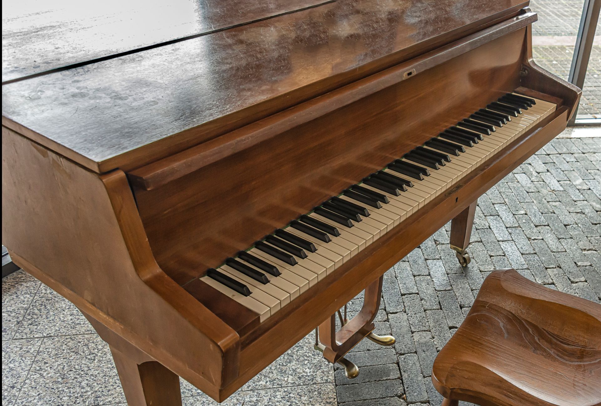 A piano is sitting on a brick floor in front of a window