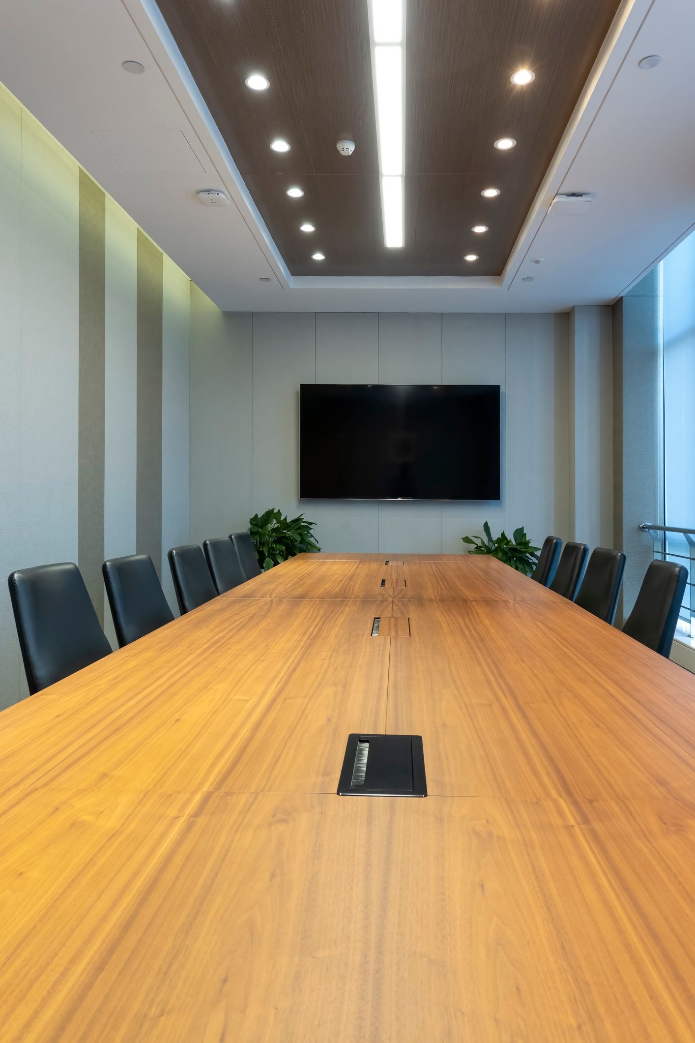 A conference room with a long wooden table and chairs and a flat screen tv.