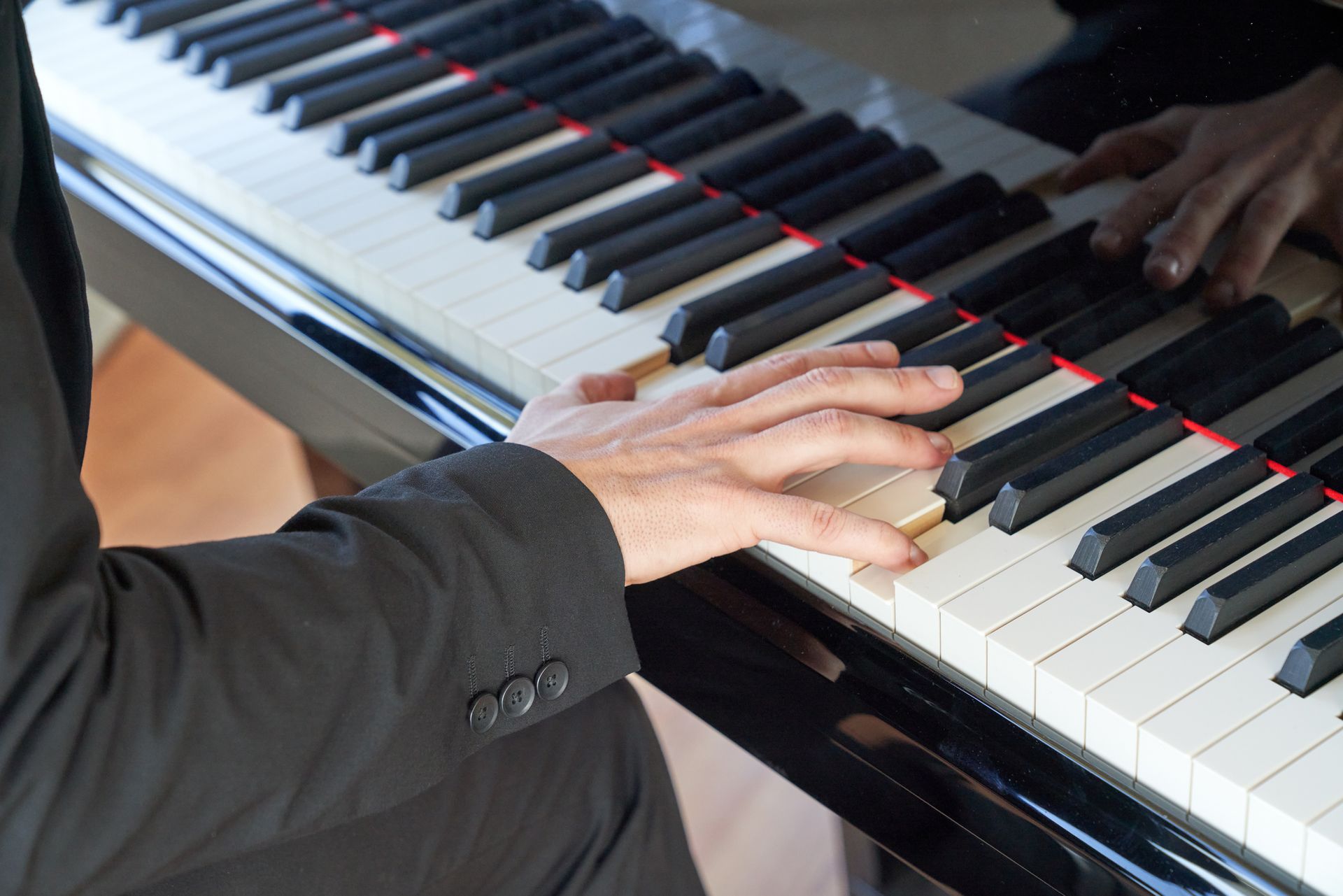 A man in a suit is playing a piano with his hands on the keys.