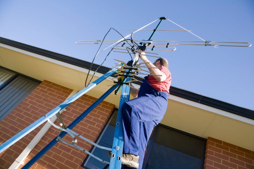 A Man Is Sitting On A Ladder Working On An Antenna — Joytech In Ciccone, NT