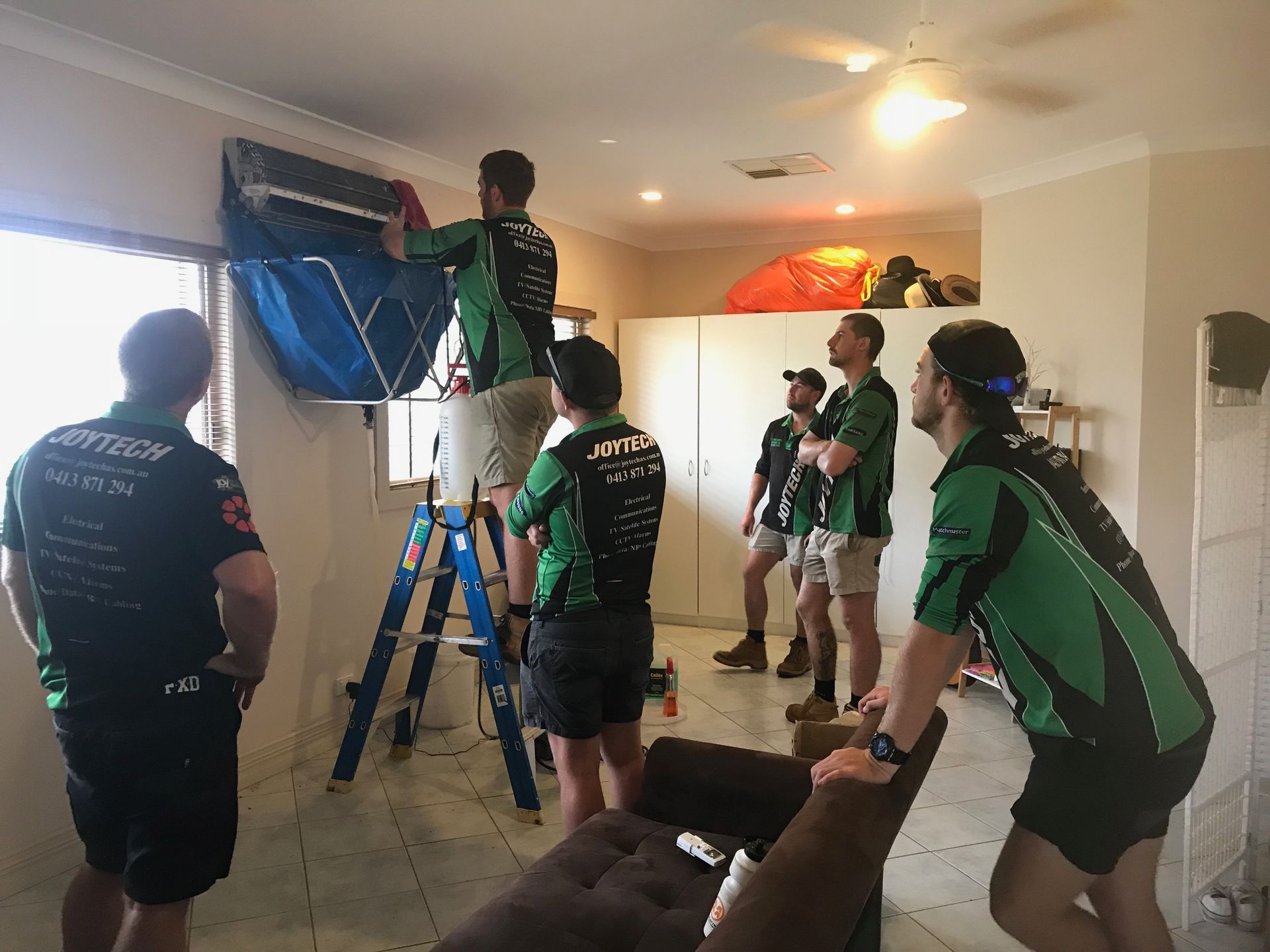 A Group Of Men Are Working On An Air Conditioner In A Living Room — Joytech In Ciccone, NT