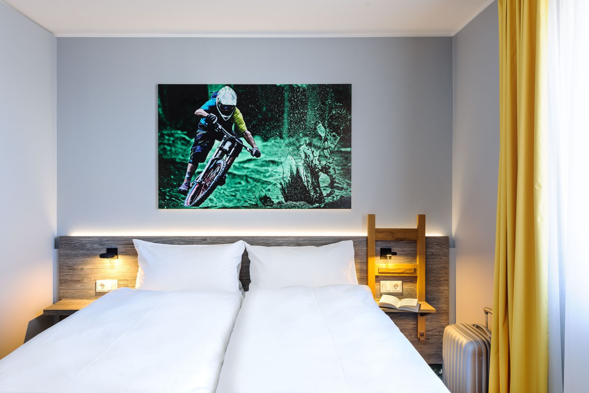 Modernes Schlafzimmer mit zwei Einzelbetten, Holzkopfteil, Wandbildern und gelben Vorhängen.