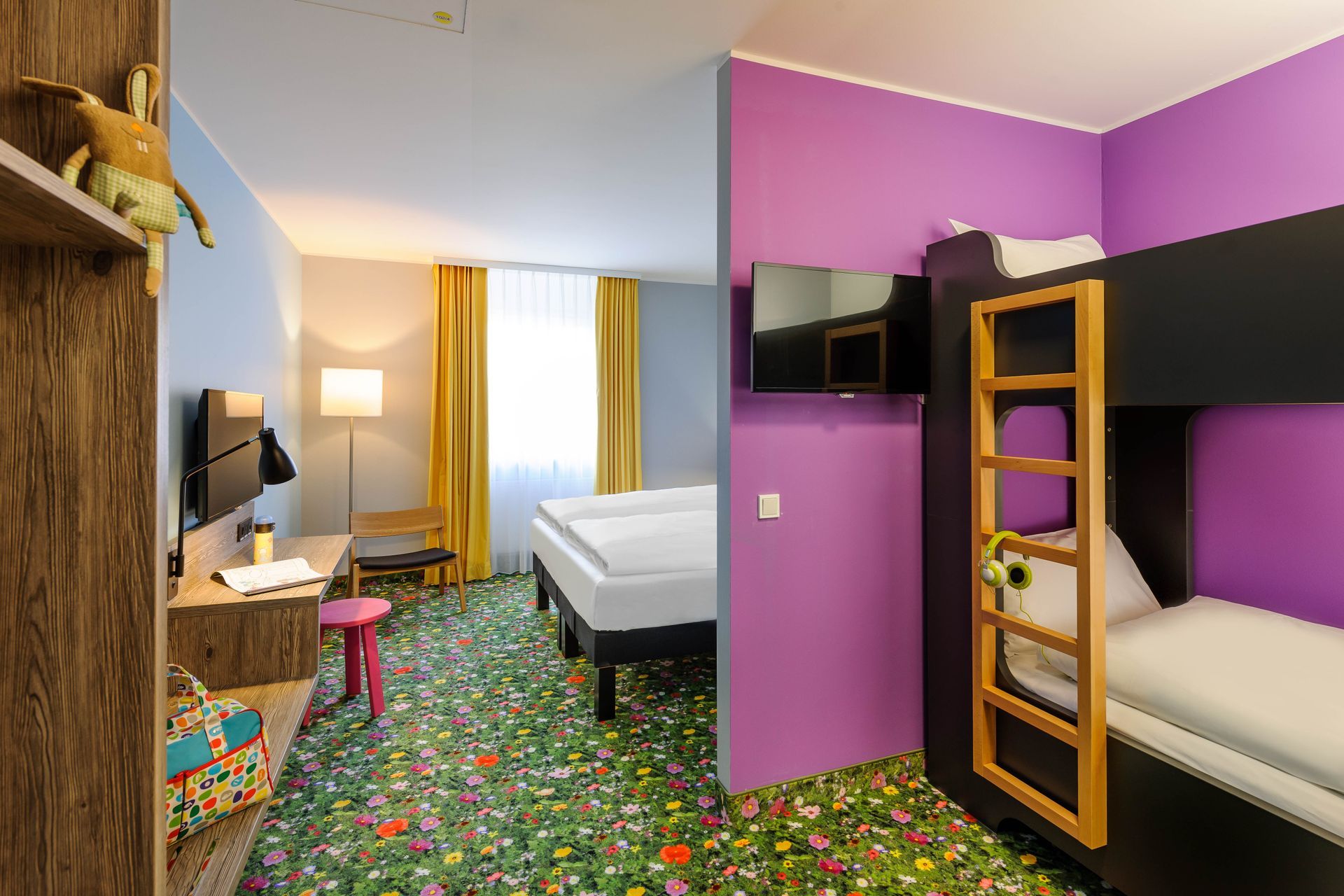 Farbenfrohes Hotelzimmer mit Etagenbetten, einem Einzelbett, Schreibtisch und lila Wänden