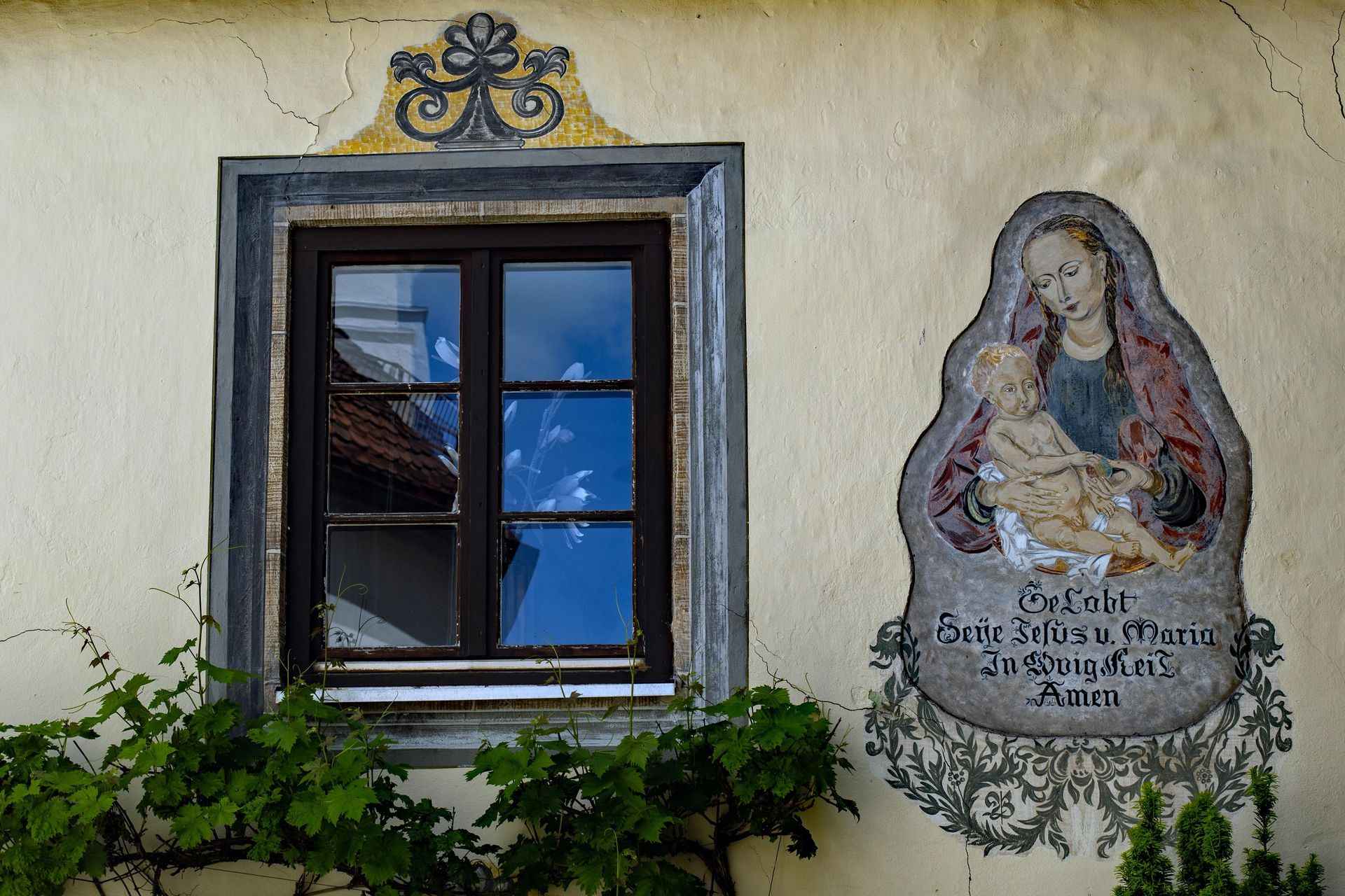 Wand mit gerahmtem Fenster, dekorativem Wappen und einem religiösen Wandgemälde mit italienischem Text und Efeu darunter