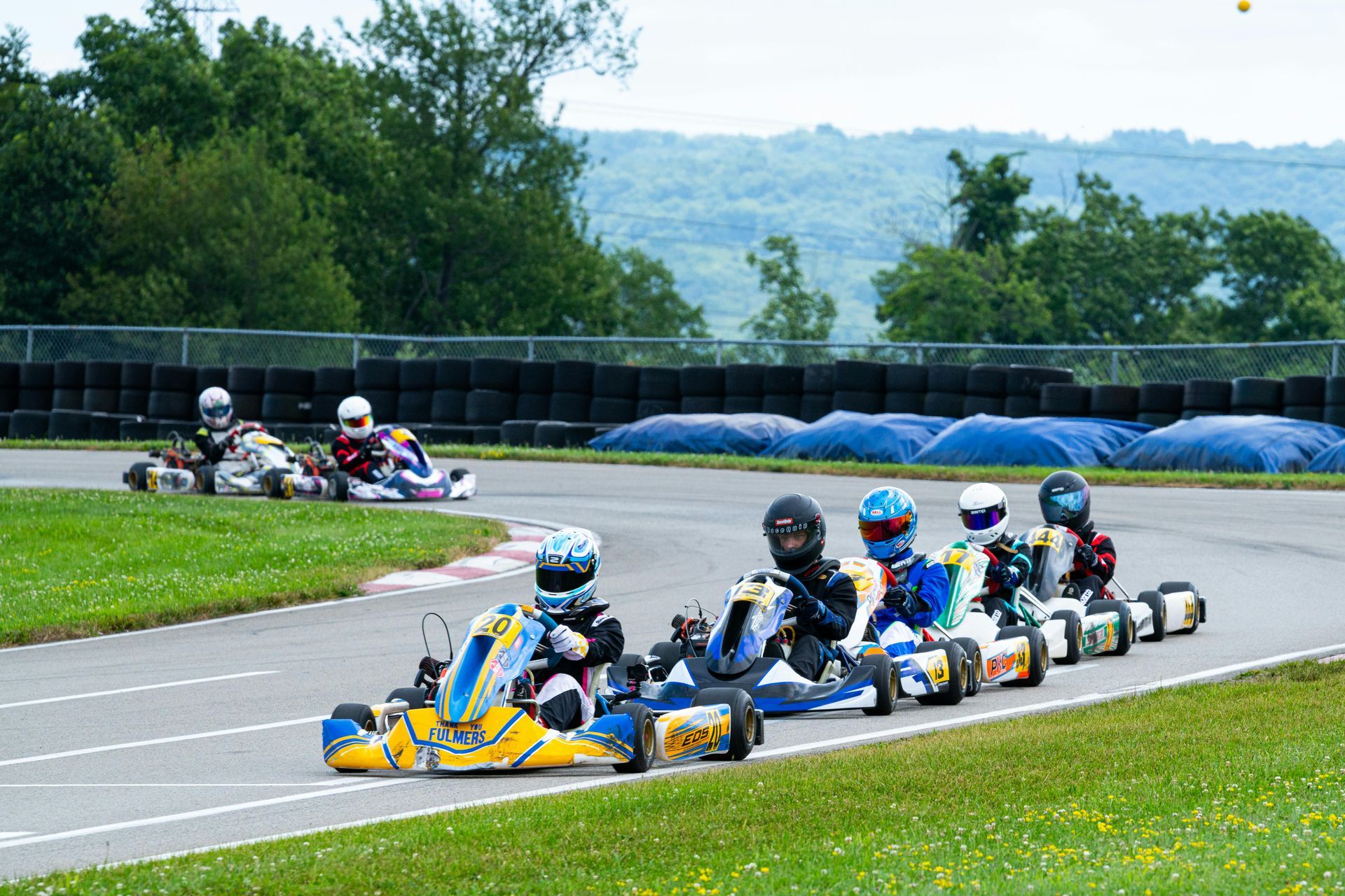 Go-kart race on a curved track, with several drivers in blue and yellow karts speeding through the turn