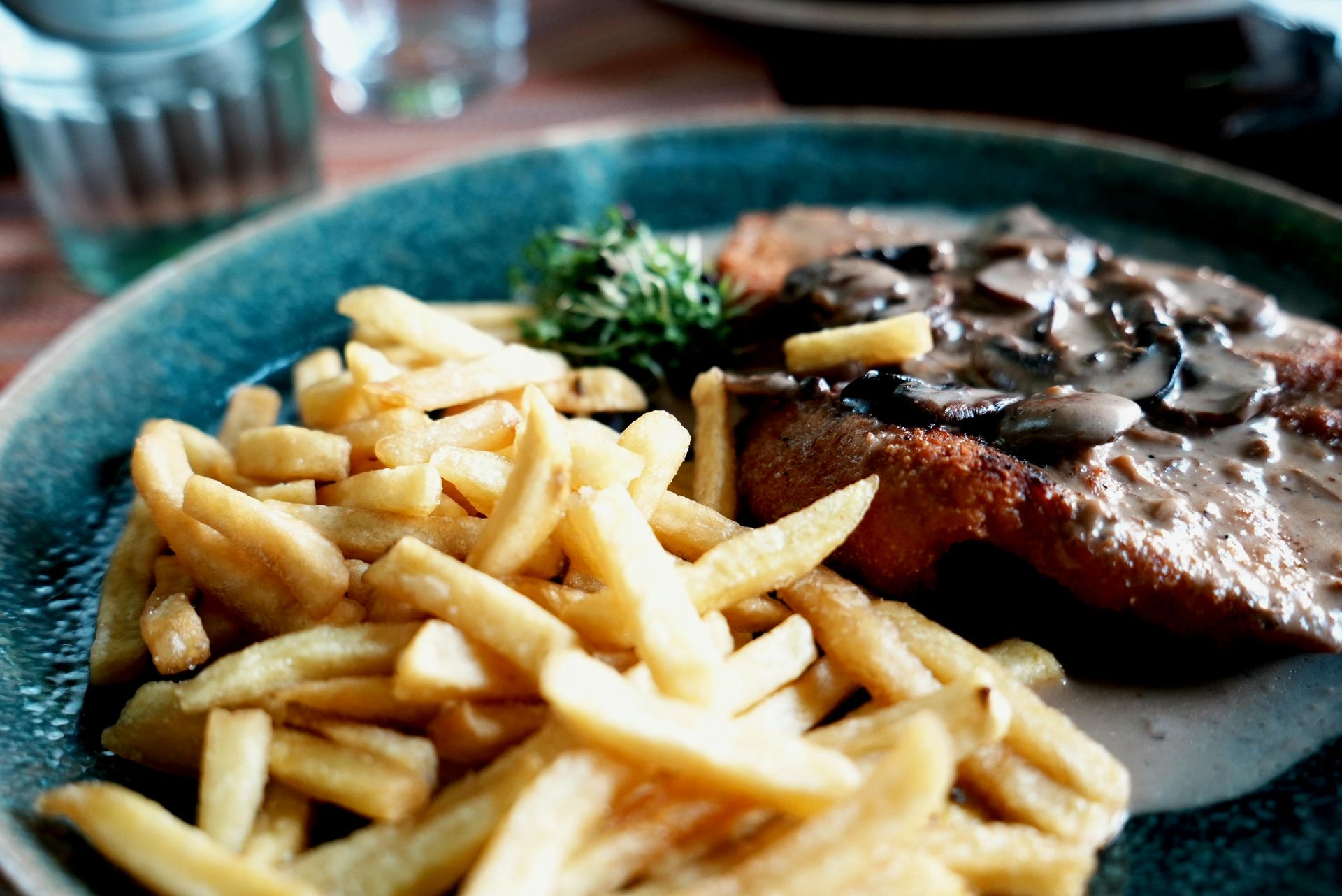 Steakteller mit Pilzsoße und Pommes frites auf einem türkisfarbenen Teller
