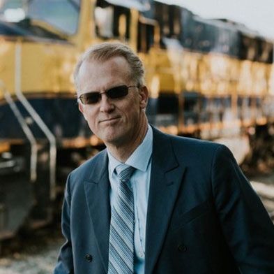 A man in a suit and tie is standing in front of a train