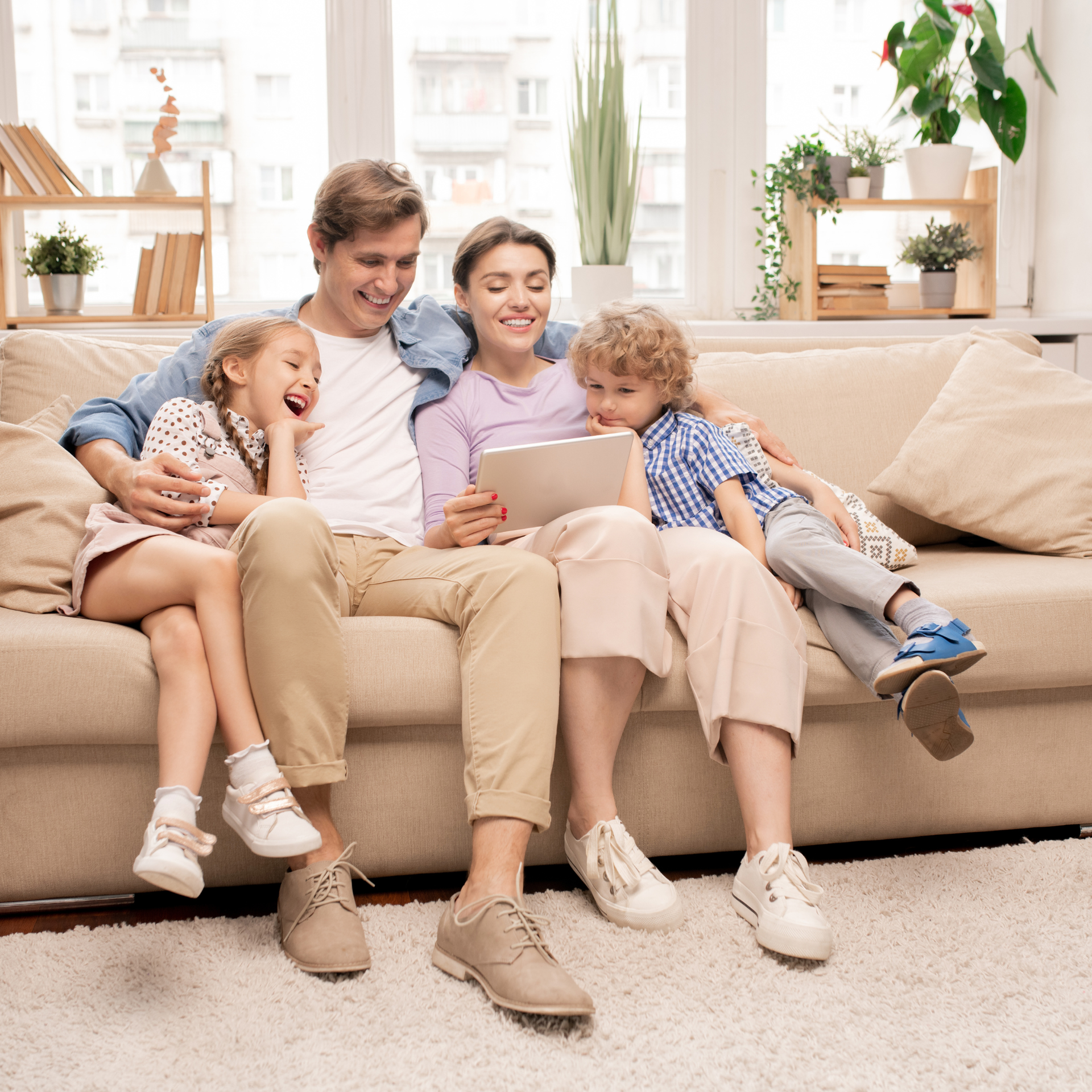 Durango HVAC Services - Family seated on couch, looking at tablet, smiling. Living room setting with plants.