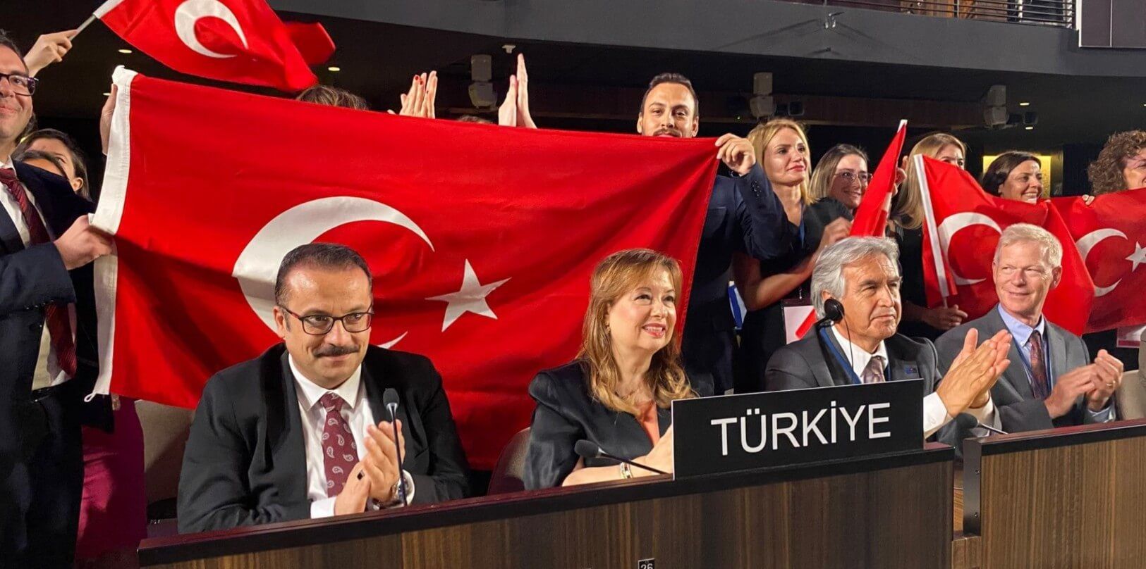 Turkish delegates celebrating in the UNESCO conference room, holding Turkish flags