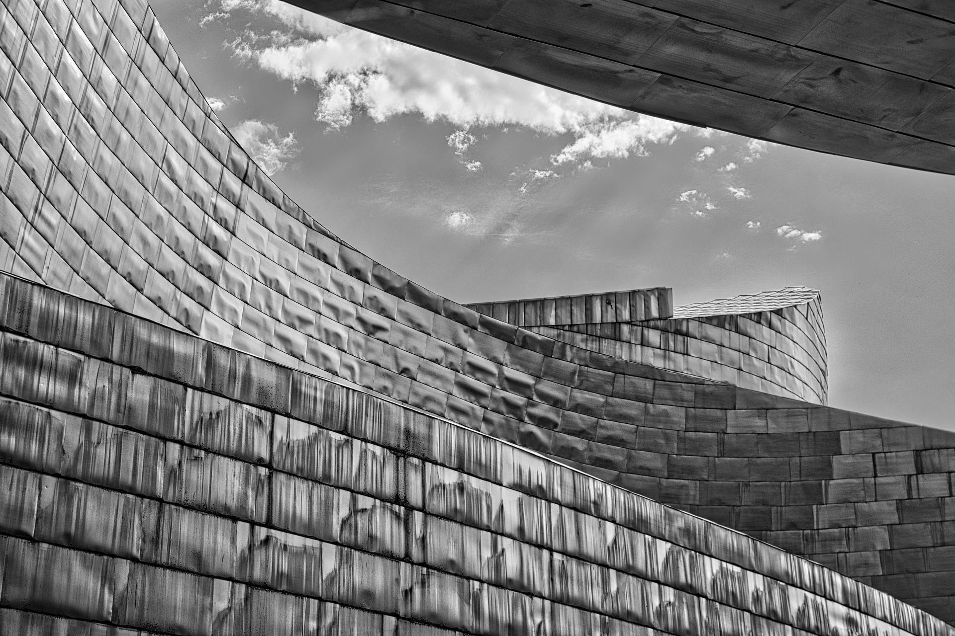 Curved stone and metal architectural walls under a cloudy sky