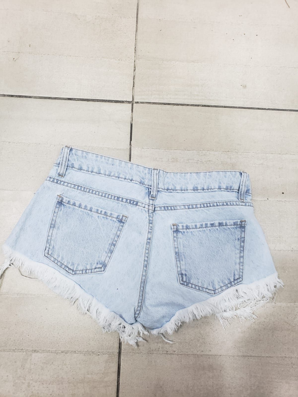 Pantalones cortos de mezclilla de lavado claro con bordes deshilachados, colocados sobre una superficie de baldosas.