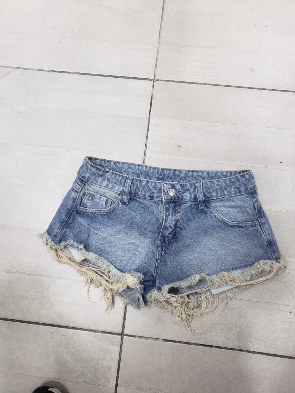Pantalones cortos de mezclilla con dobladillos deshilachados sobre un suelo de baldosas.