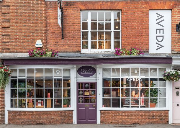 Salon Cabelo – an Aveda hair salon with a stylish storefront, large windows, and luxury hair products. Located in a charming brick building with flower displays.