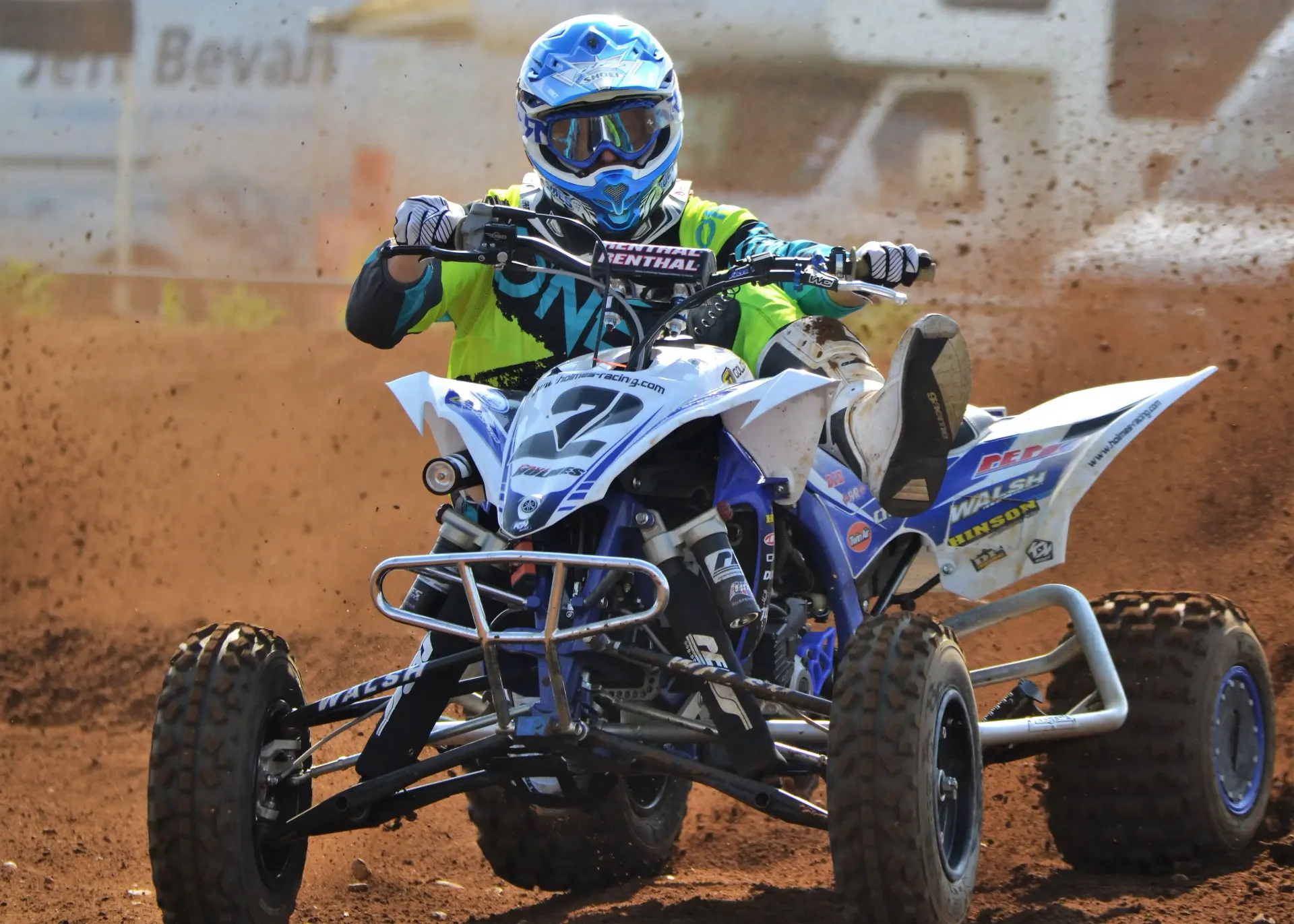ATV racer on a dusty dirt track, wearing a helmet, leaning into a turn.
