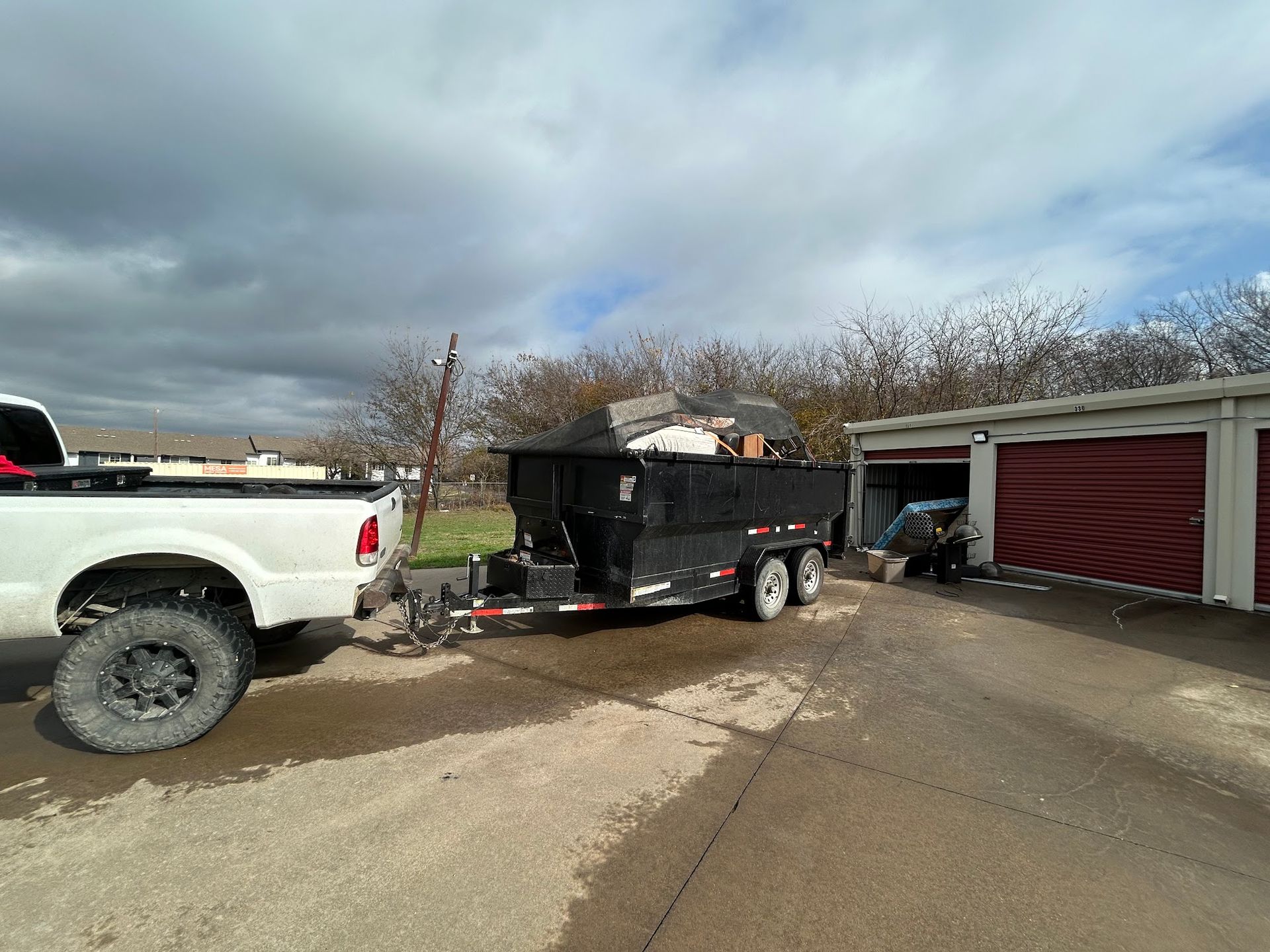 A white truck is towing a black dump trailer.