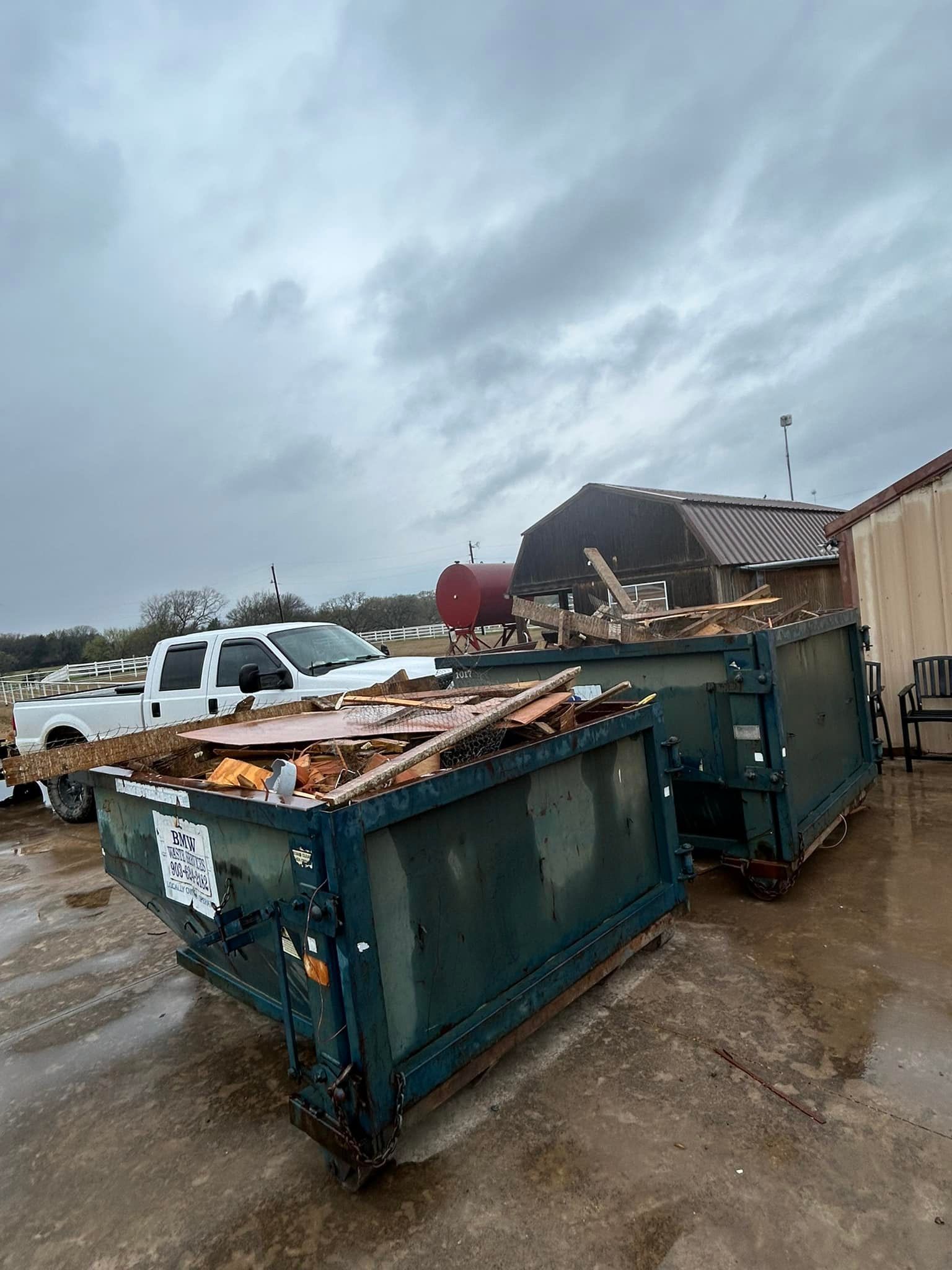 A white truck with an american flag on the back is parked in front of a dumpster.