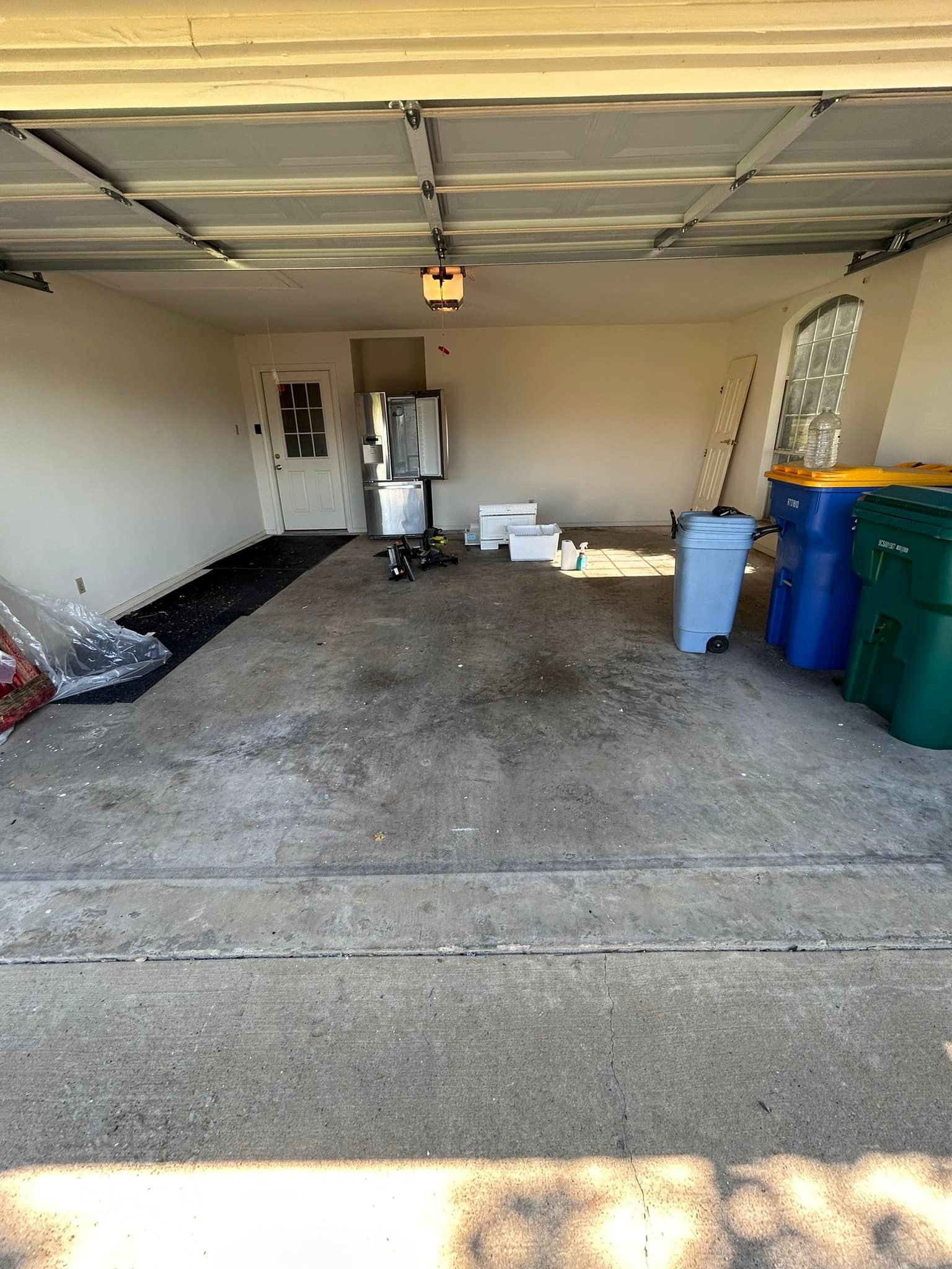 A garage filled with trash cans and a refrigerator.