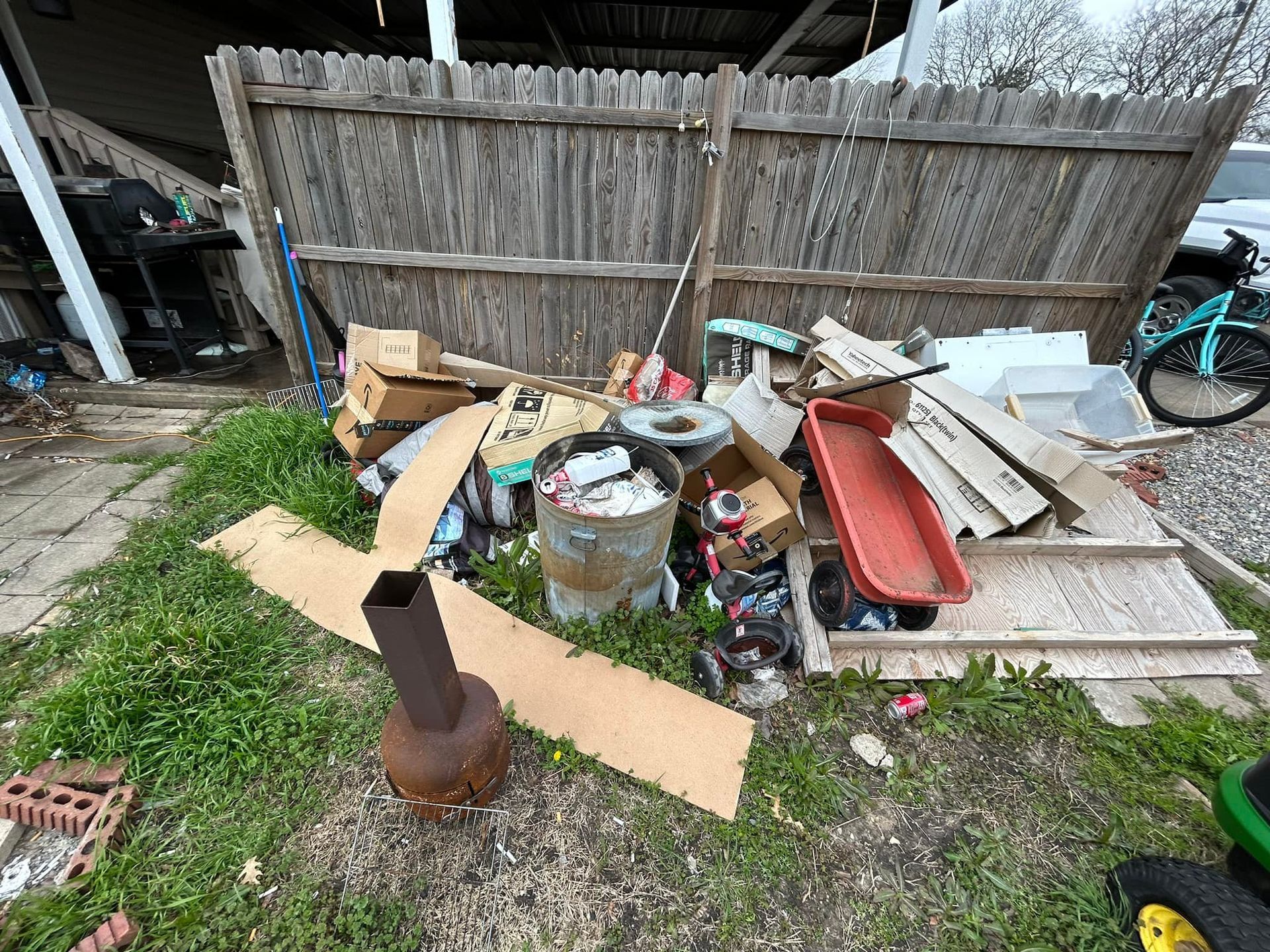 A pile of trash is sitting in the grass in front of a wooden fence.