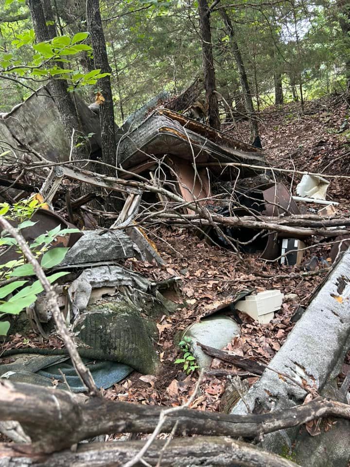 A pile of trash is laying on the ground in the woods.