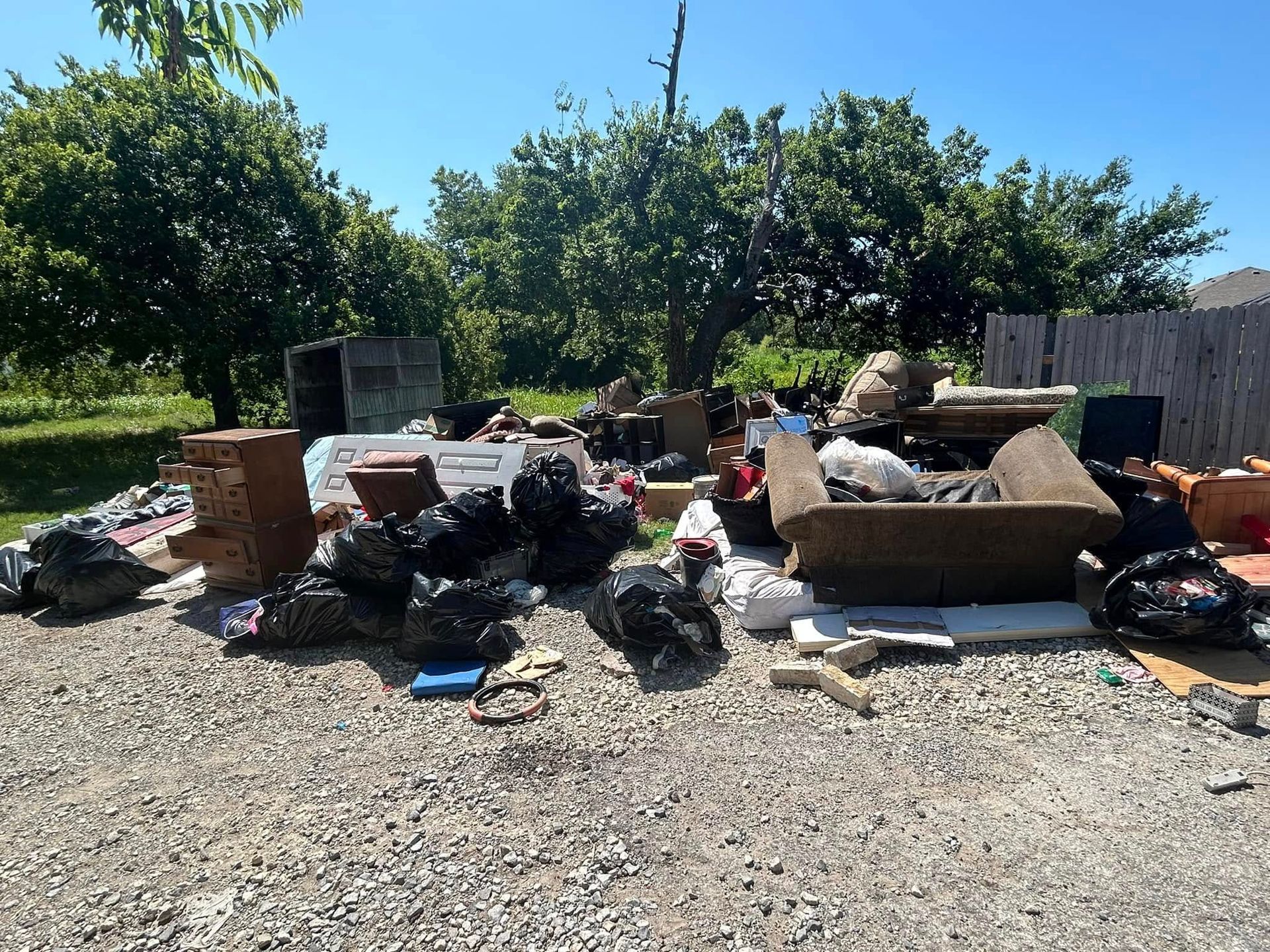 A pile of trash in a gravel area with trees in the background