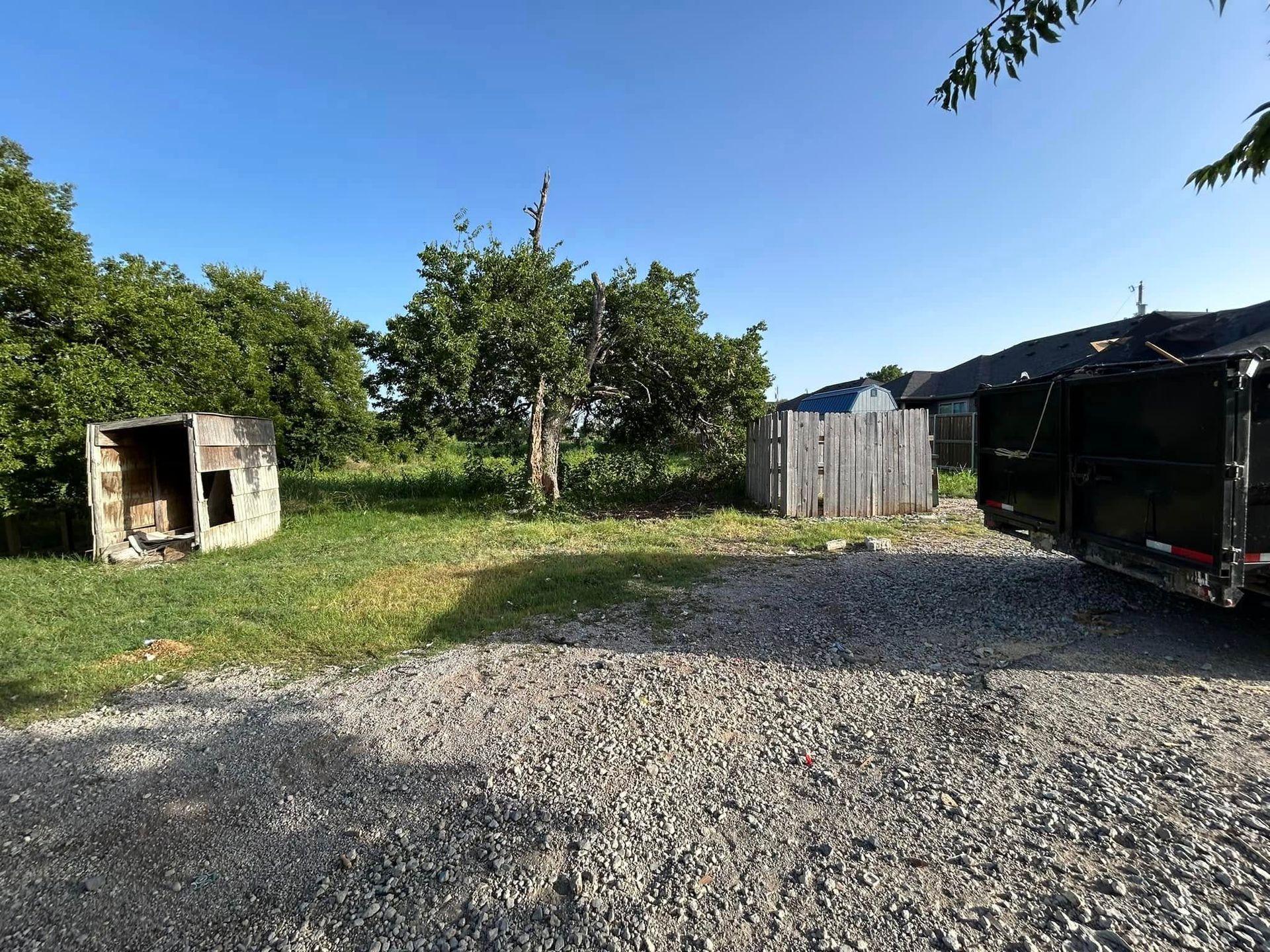A trailer is parked in a gravel lot next to a dog house.
