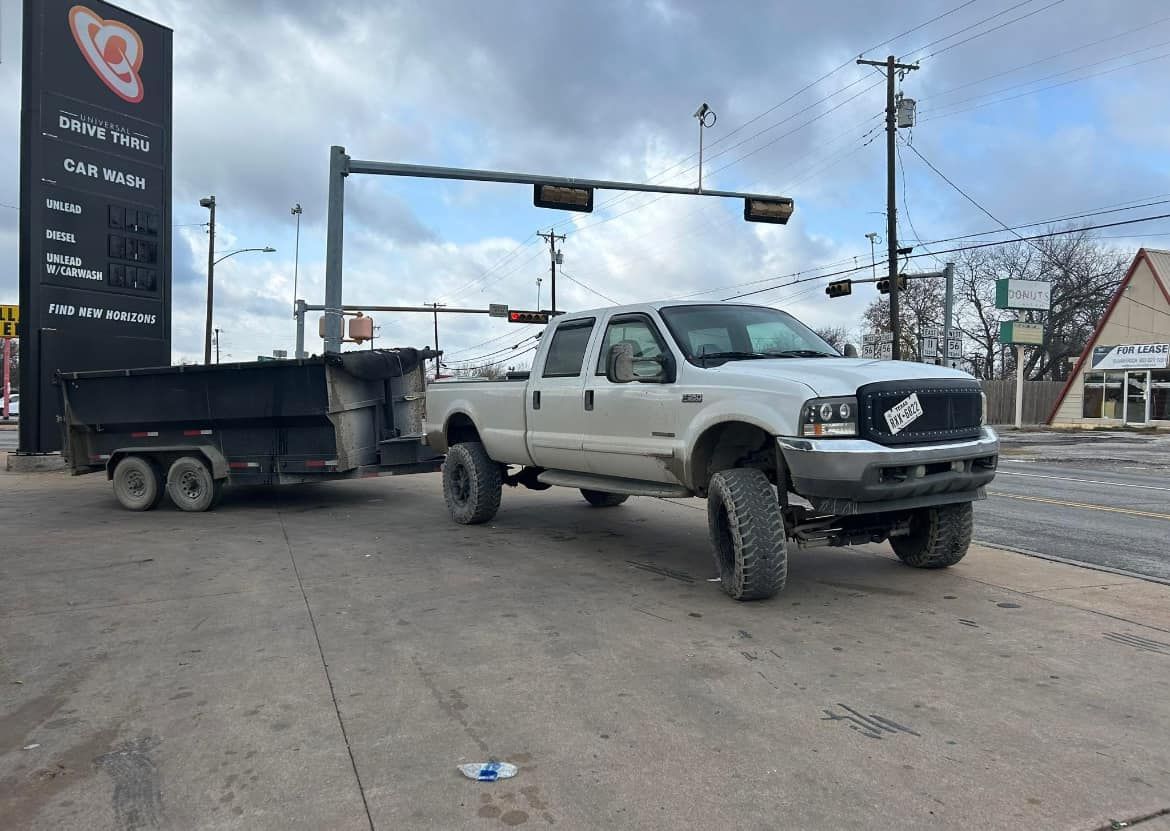 A white truck with a dump trailer attached to it is parked in a parking lot.