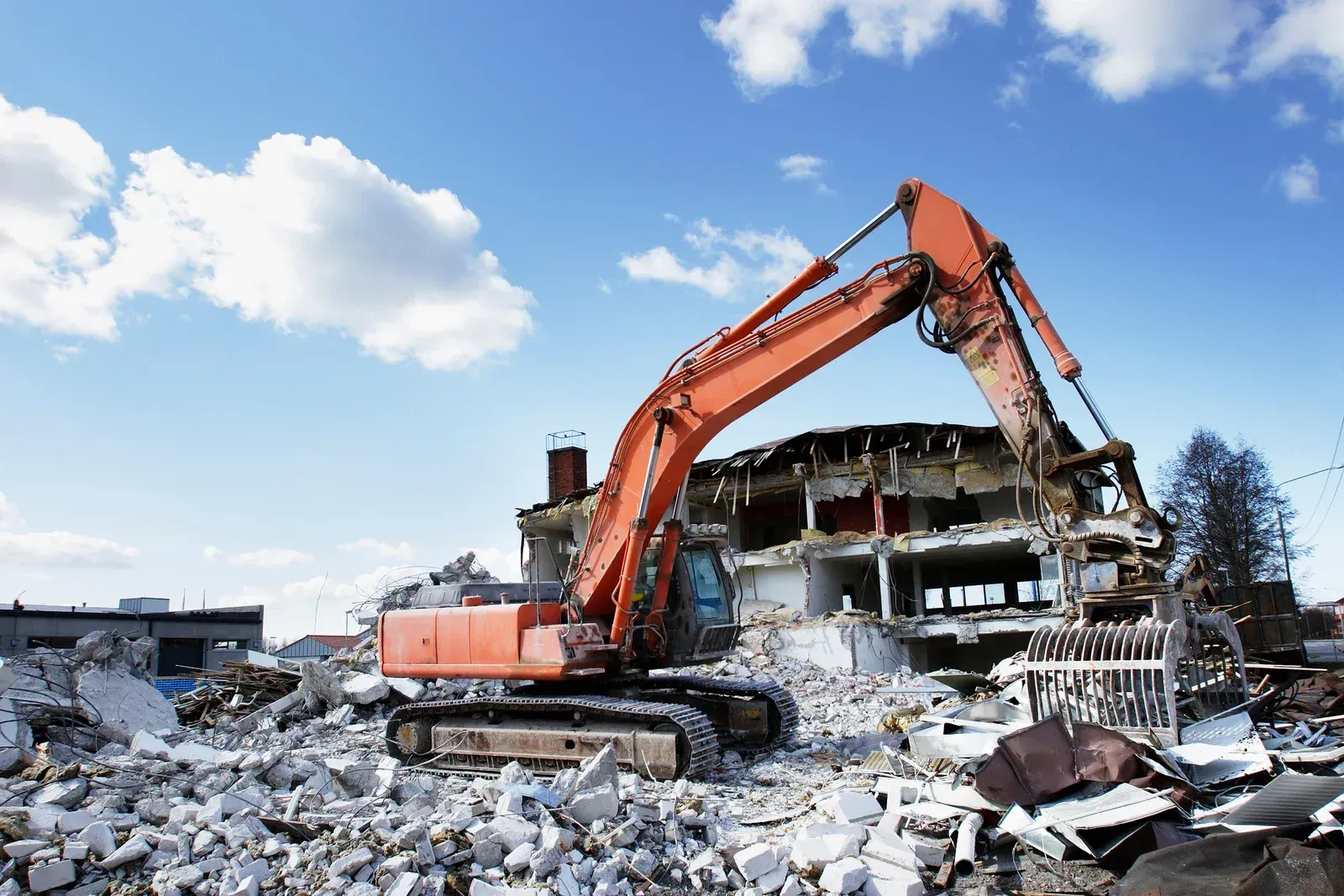 A large orange excavator is demolishing a building.