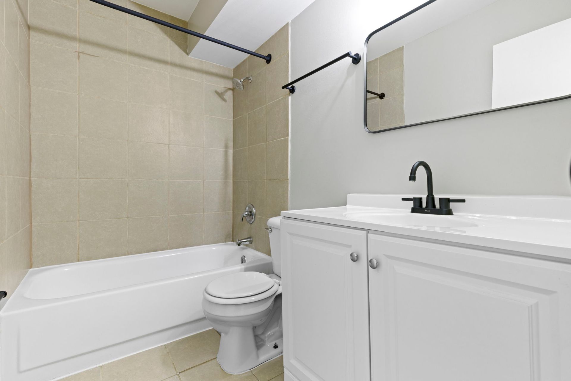 Bathroom with white vanity, tub, toilet, and beige tile. Black fixtures and a mirror.