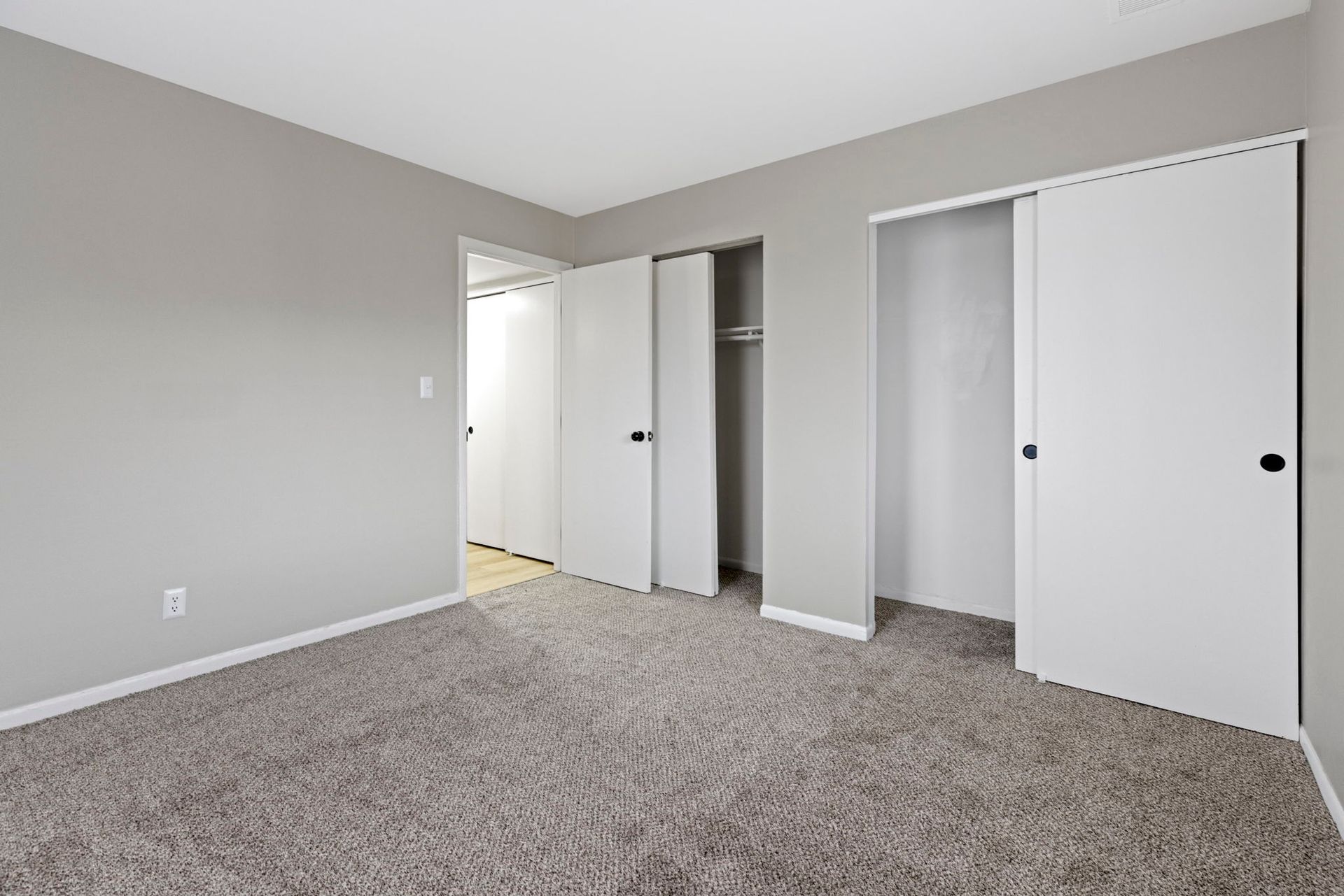 Empty bedroom with grey walls, carpet, and white closet doors.
