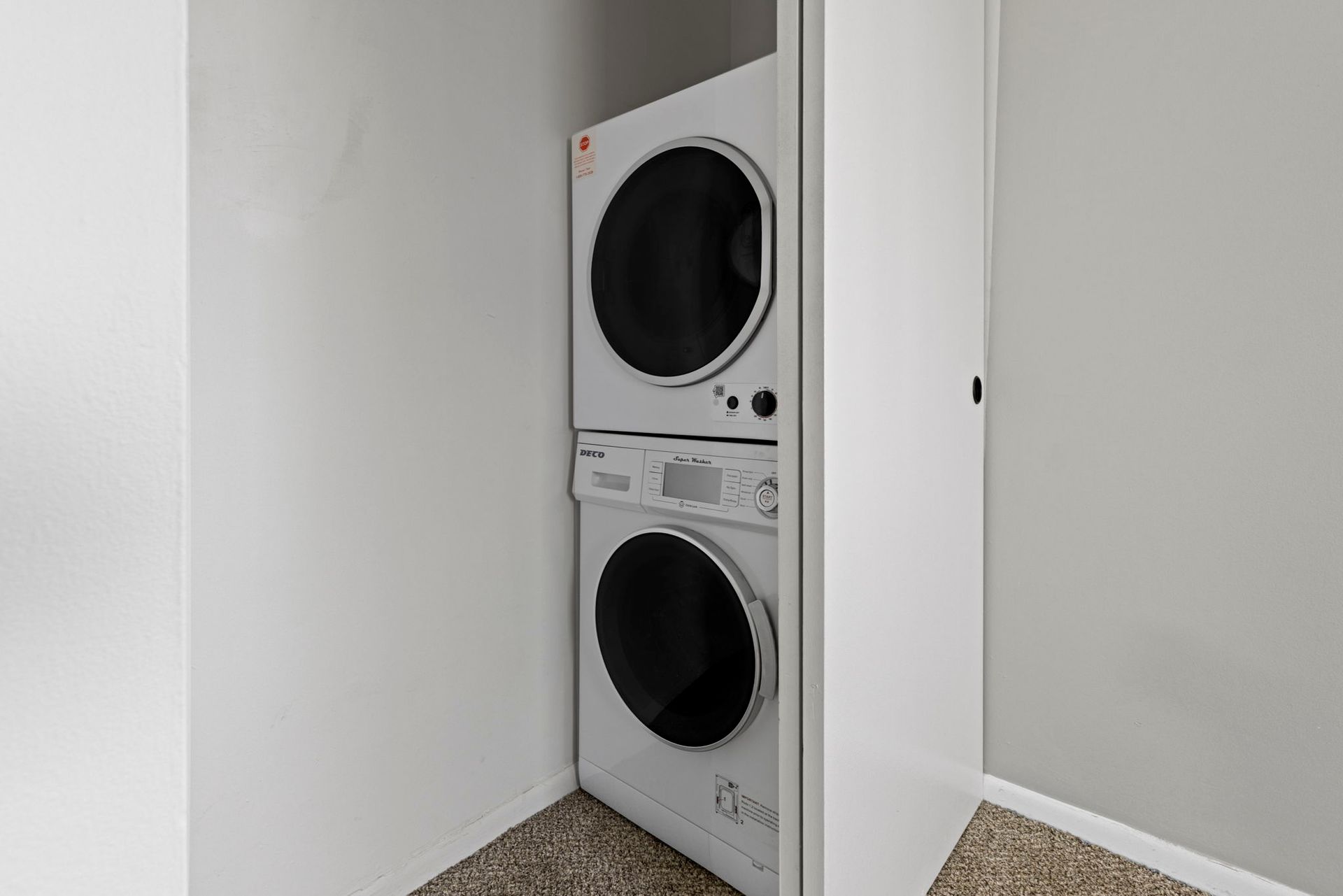 Stacked white washer and dryer inside a white closet with a beige carpet.