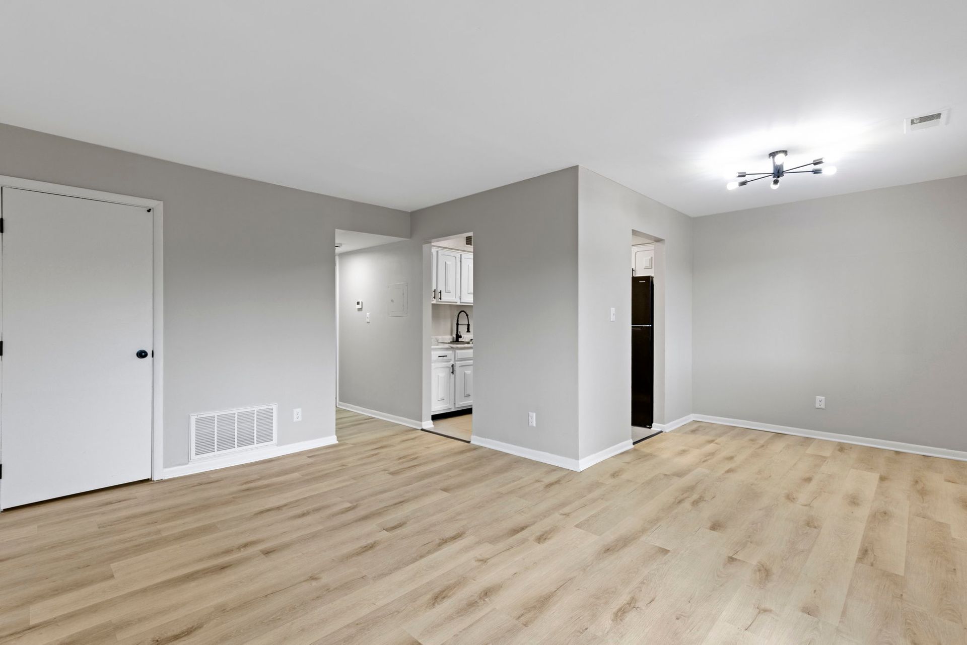 Empty living room with light wood flooring, gray walls, and white trim.