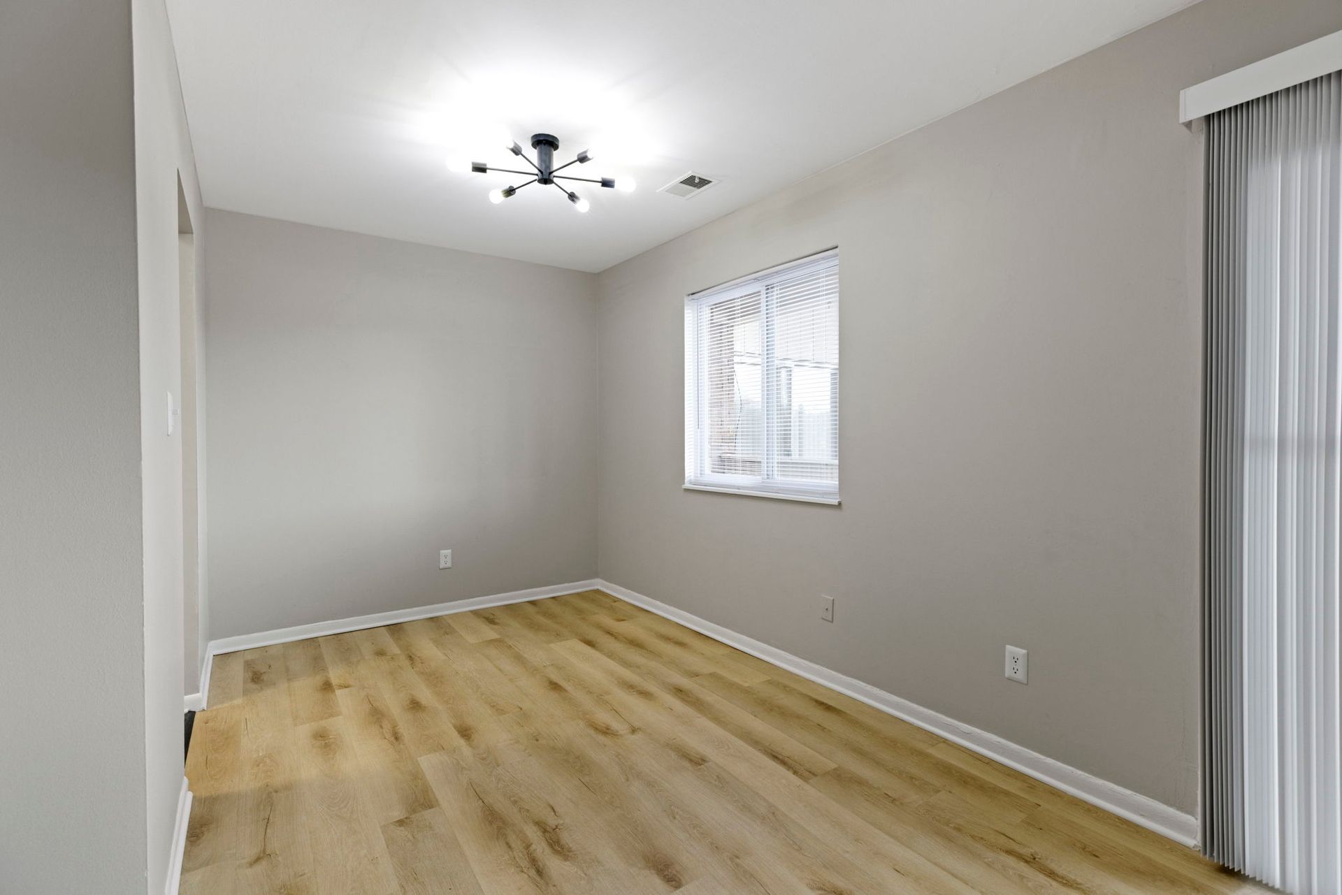 Empty room with wood-look floors, white walls, window with blinds, and a light fixture.