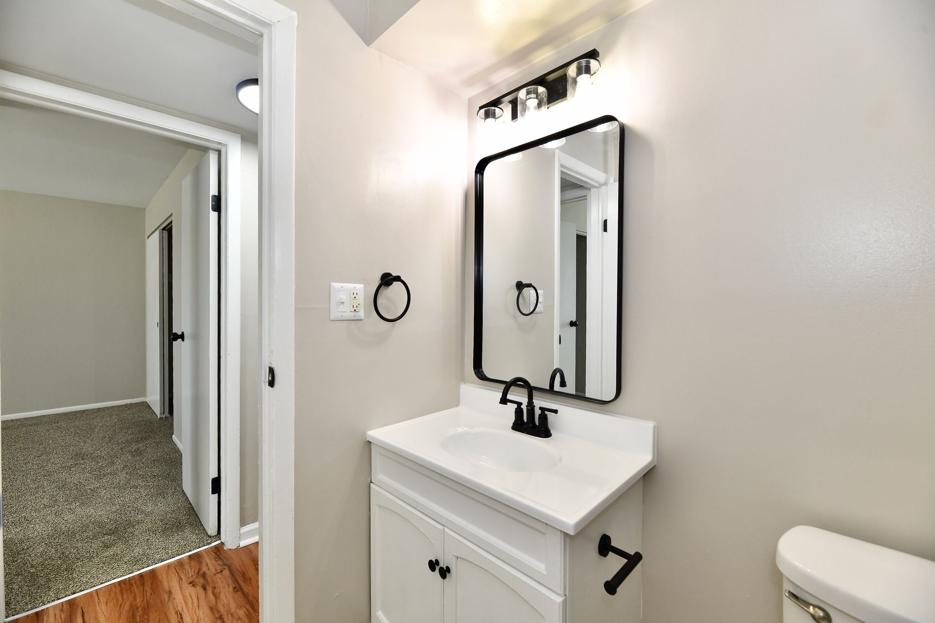 Bathroom with white vanity, black mirror, and open doorway to hallway with carpet.