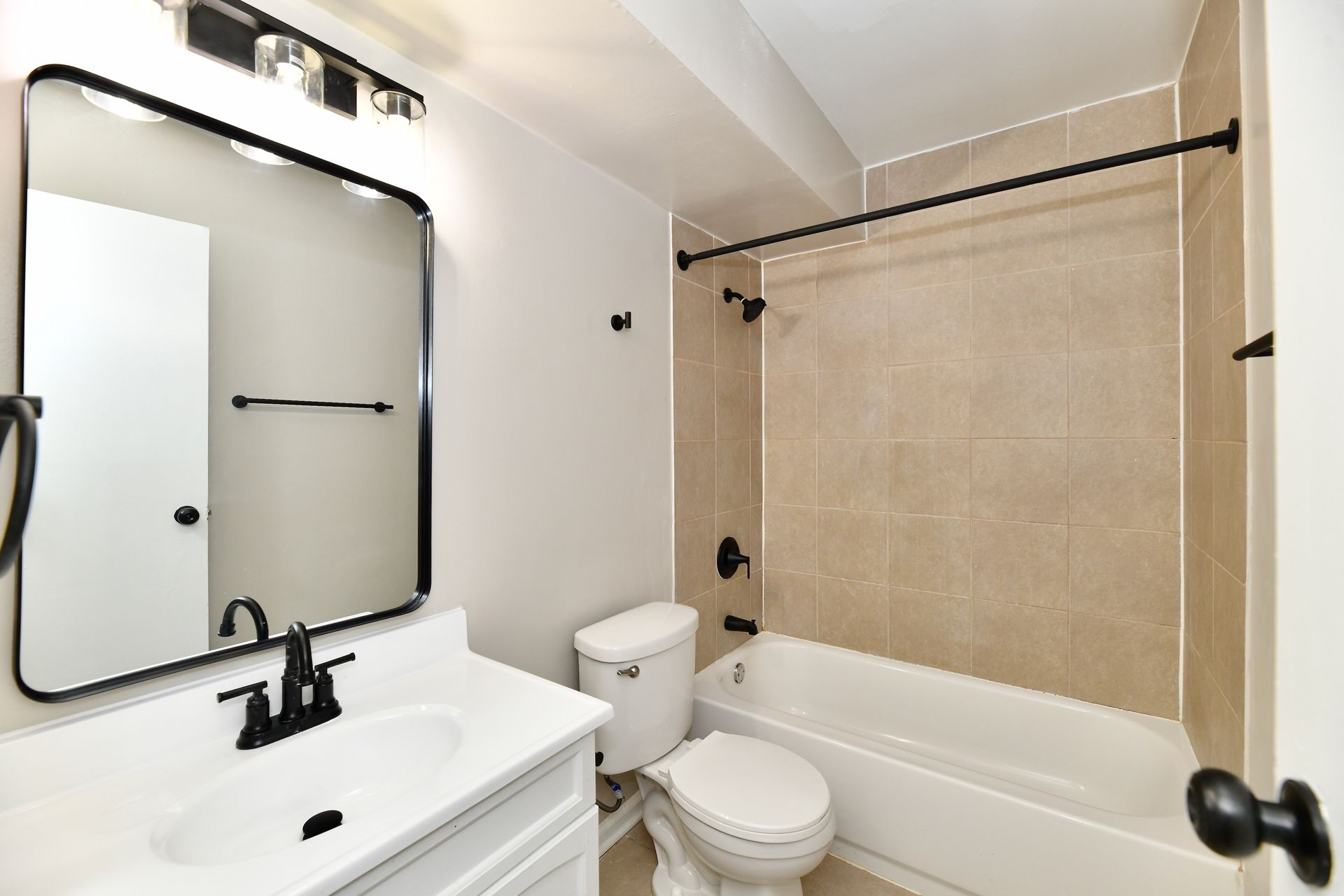 Bathroom with beige tile, white fixtures, black hardware, and a large mirror.
