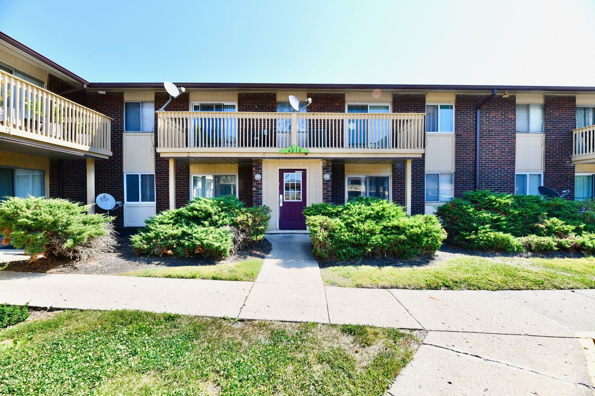 Two-story apartment building with brick and beige exterior, balconies, and a purple front door.