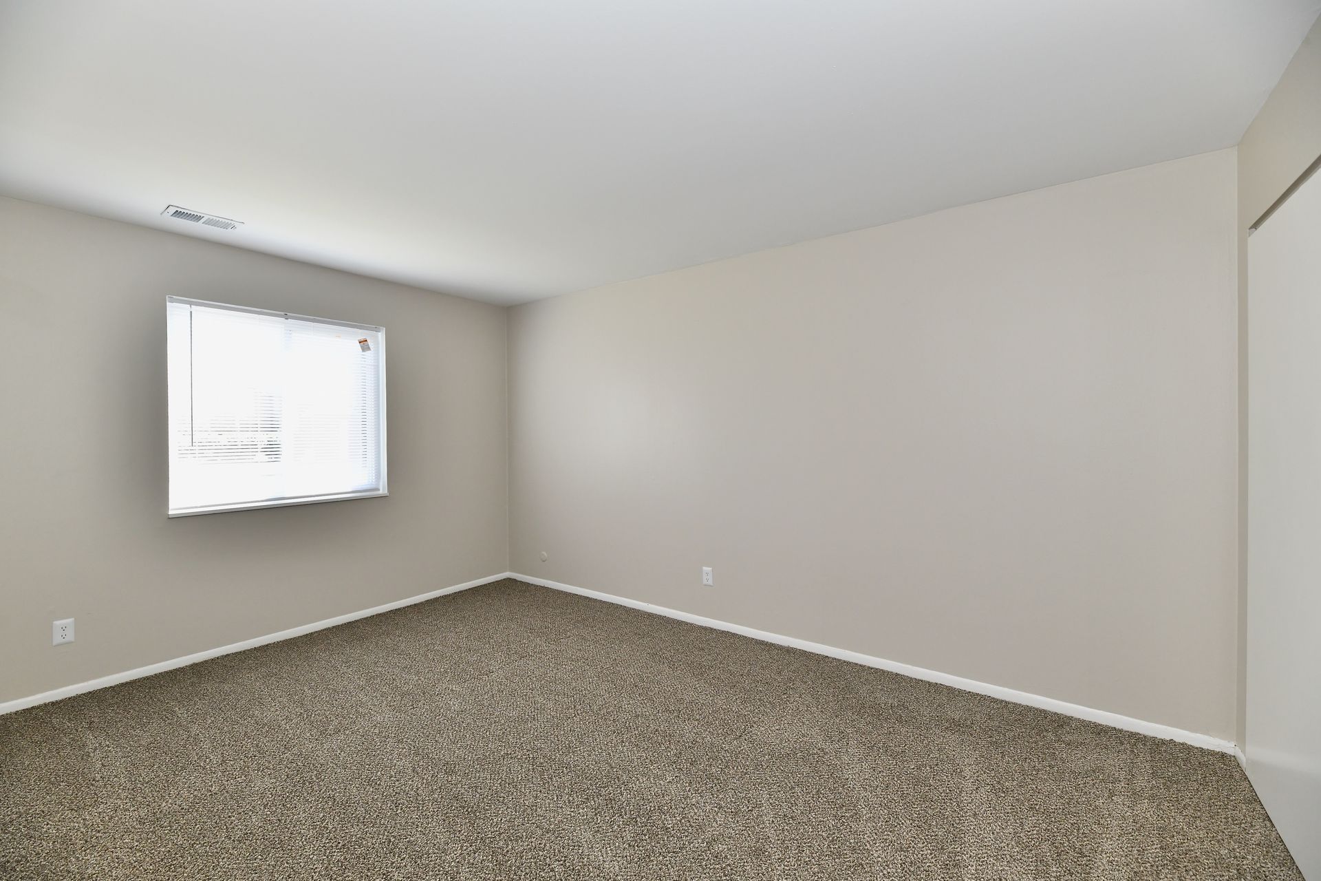 Empty room with beige walls, brown carpet, a window, and a closet door.
