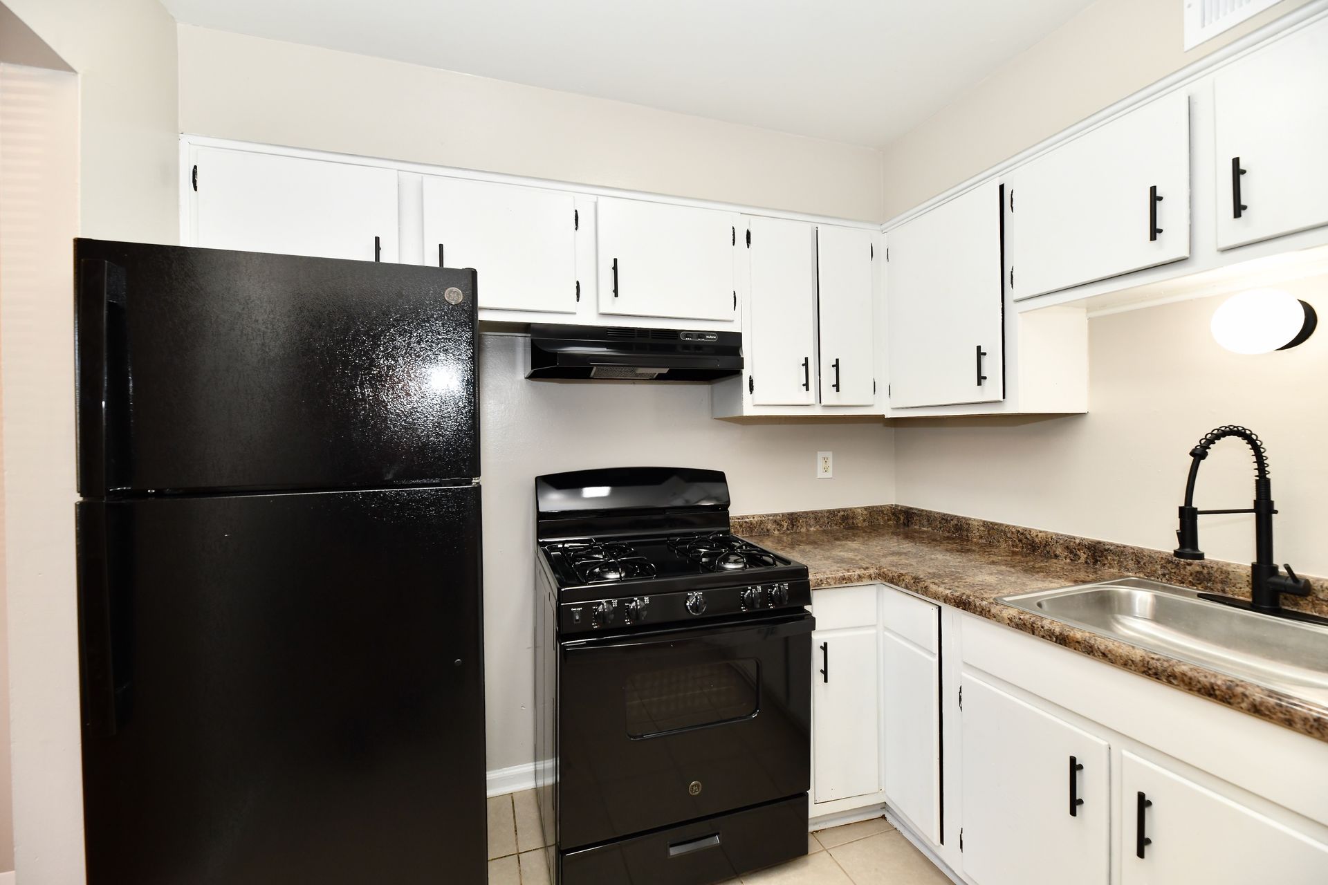 Black appliances in a white-cabineted kitchen with a brown countertop and a silver sink.