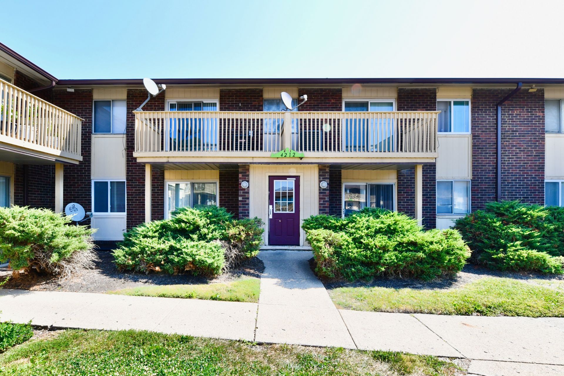 Two-story brick apartment building with balconies and a purple front door.