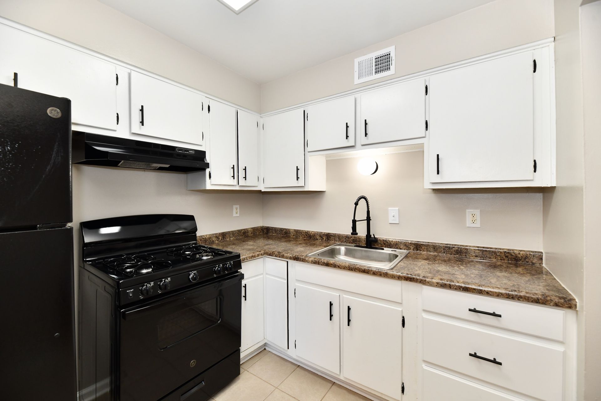 White kitchen cabinets and countertops, black appliances, and faucet.