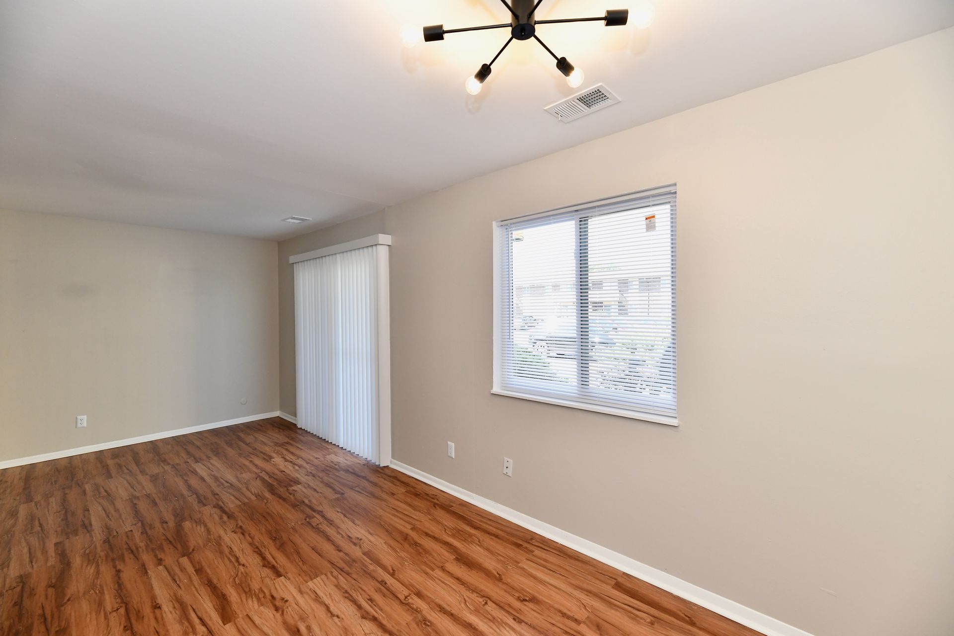 Empty room with wood-look flooring, sliding door, window, and modern light fixture.
