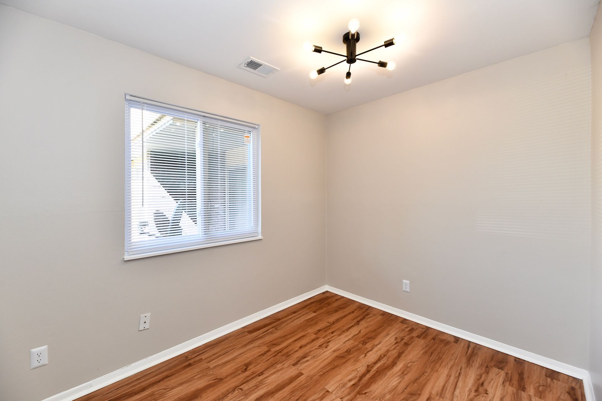 Empty room with wood-look floor, window with blinds, and a modern light fixture.