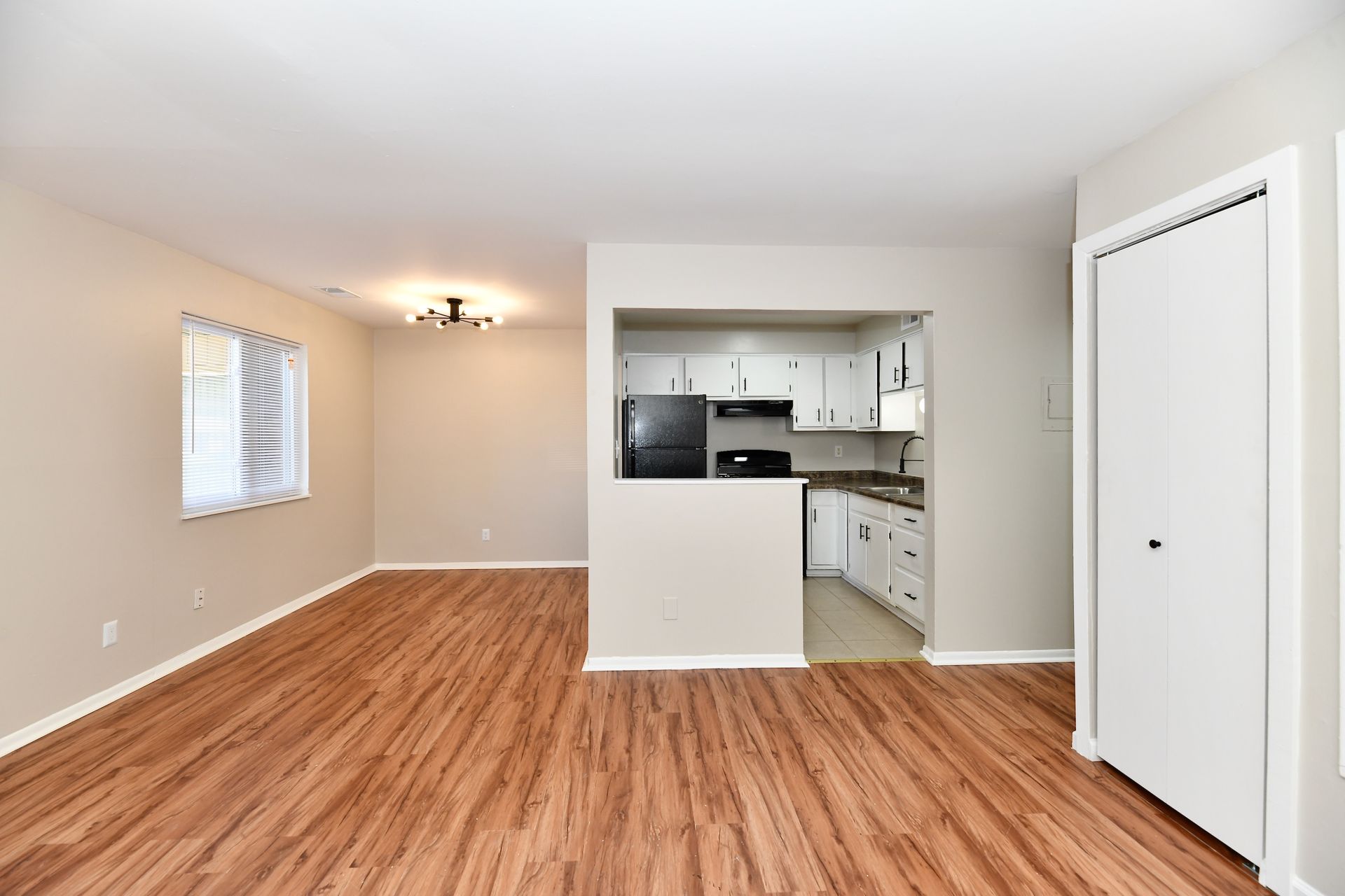 Living room with wood flooring, open to a kitchen. Includes a window, closet, and white and black appliances.