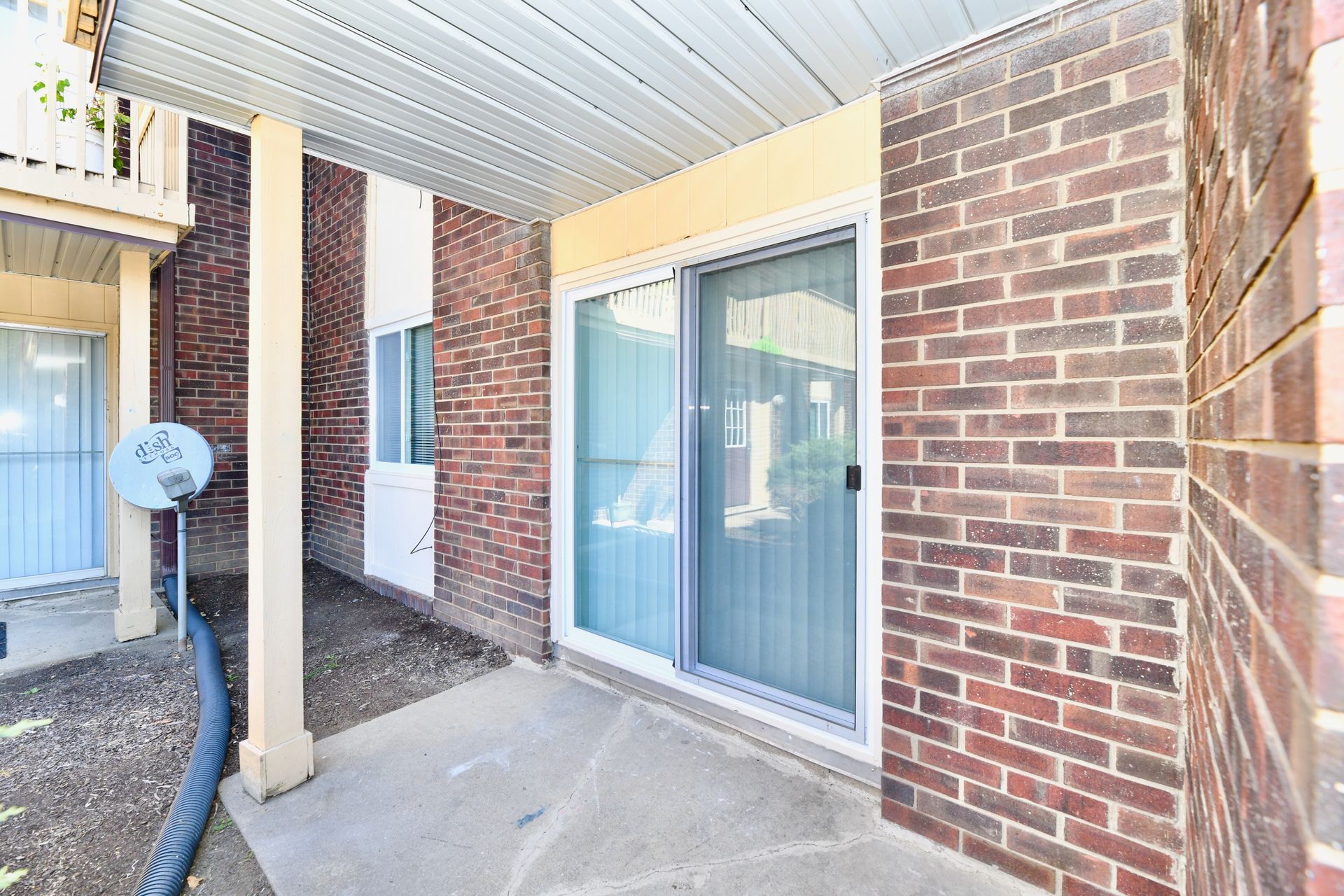 Covered patio with sliding glass door and brick wall.