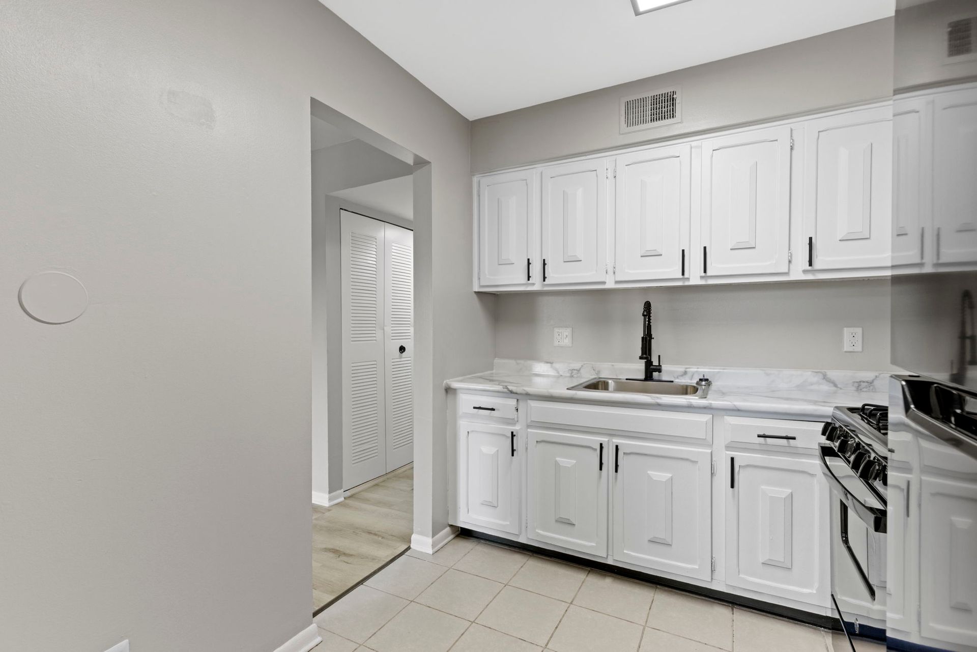 White kitchen with cabinets, sink, and a stove, next to a doorway to a hallway with a closet.