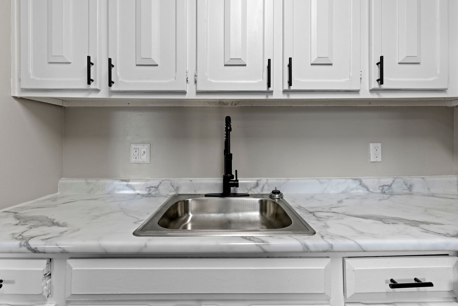 White kitchen cabinets with black hardware, countertop, and sink with a black faucet.