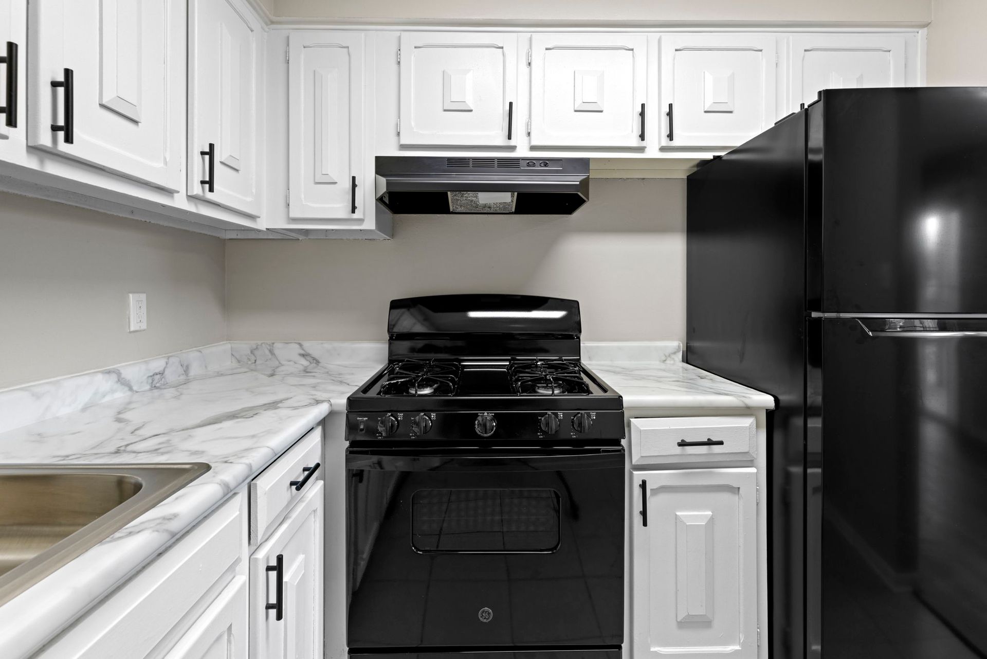 White kitchen with marble countertops, black appliances, and white cabinets.