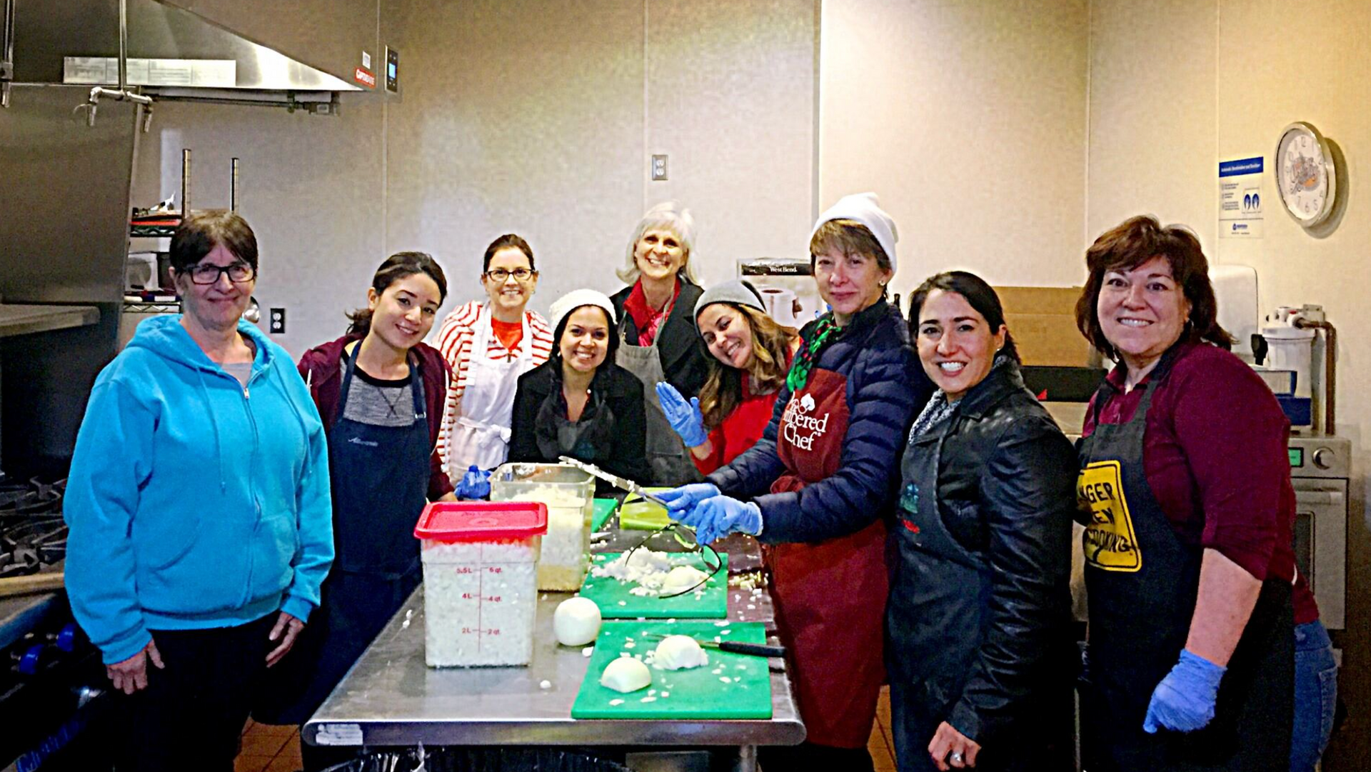 A group of women are standing around a table in a kitchen.