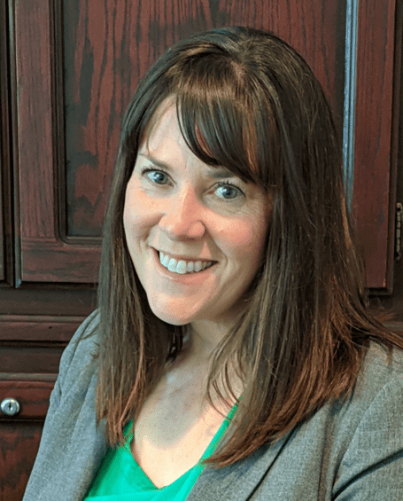 A woman in a green shirt and gray jacket is smiling for the camera.