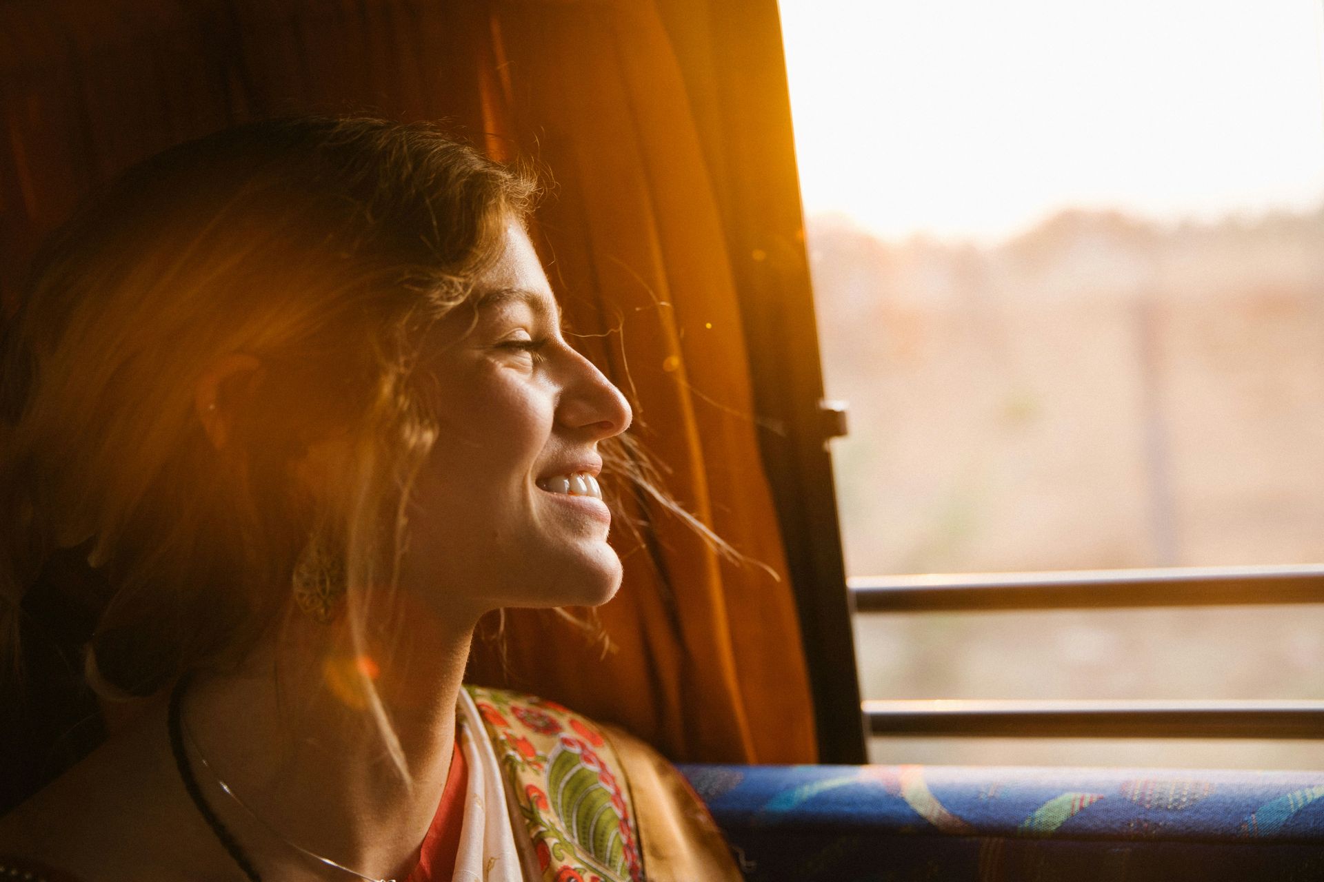 A woman is smiling while looking out of a window on a bus.