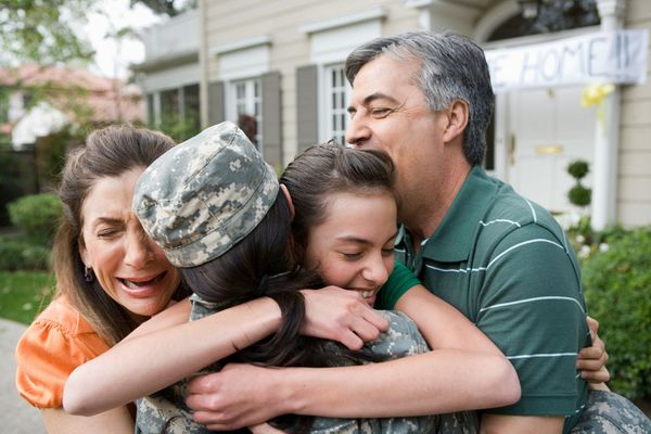 A group of people hugging a soldier in front of a house.